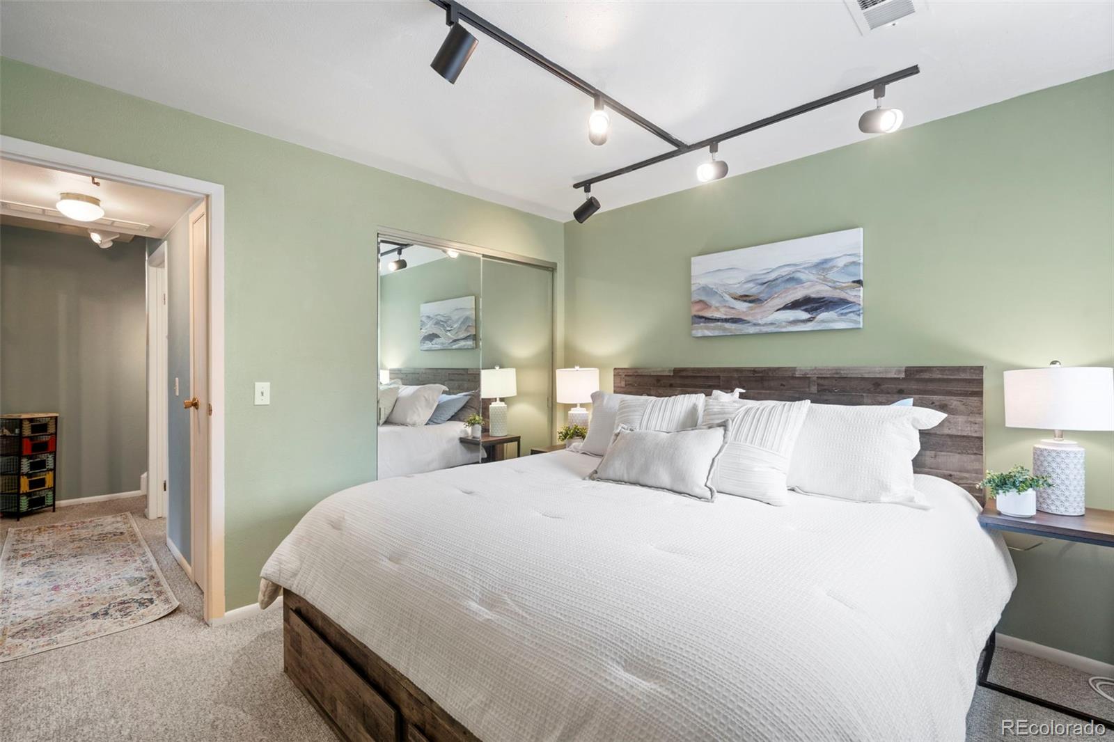 Bedroom with a large white bed, dark wood headboard, pale green walls, and mirrored closet doors.
