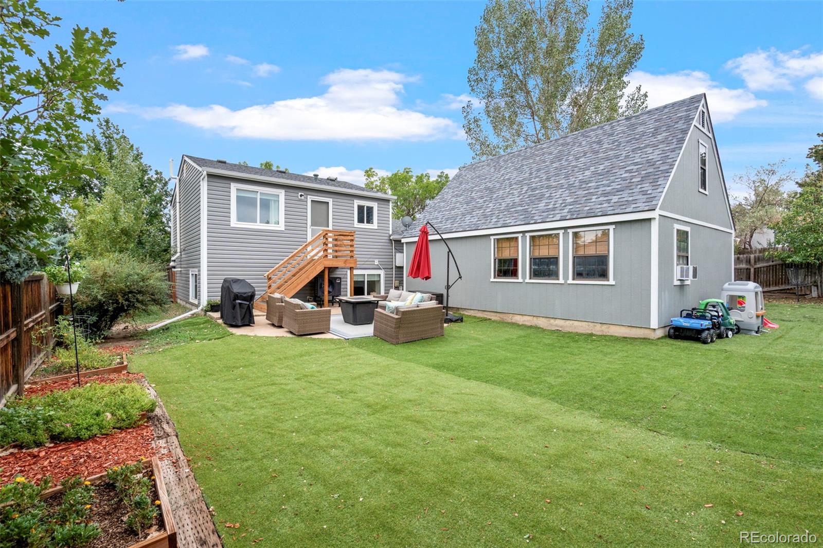 Gray two-story home with a broad backyard lawn, raised garden beds, and a furnished patio.