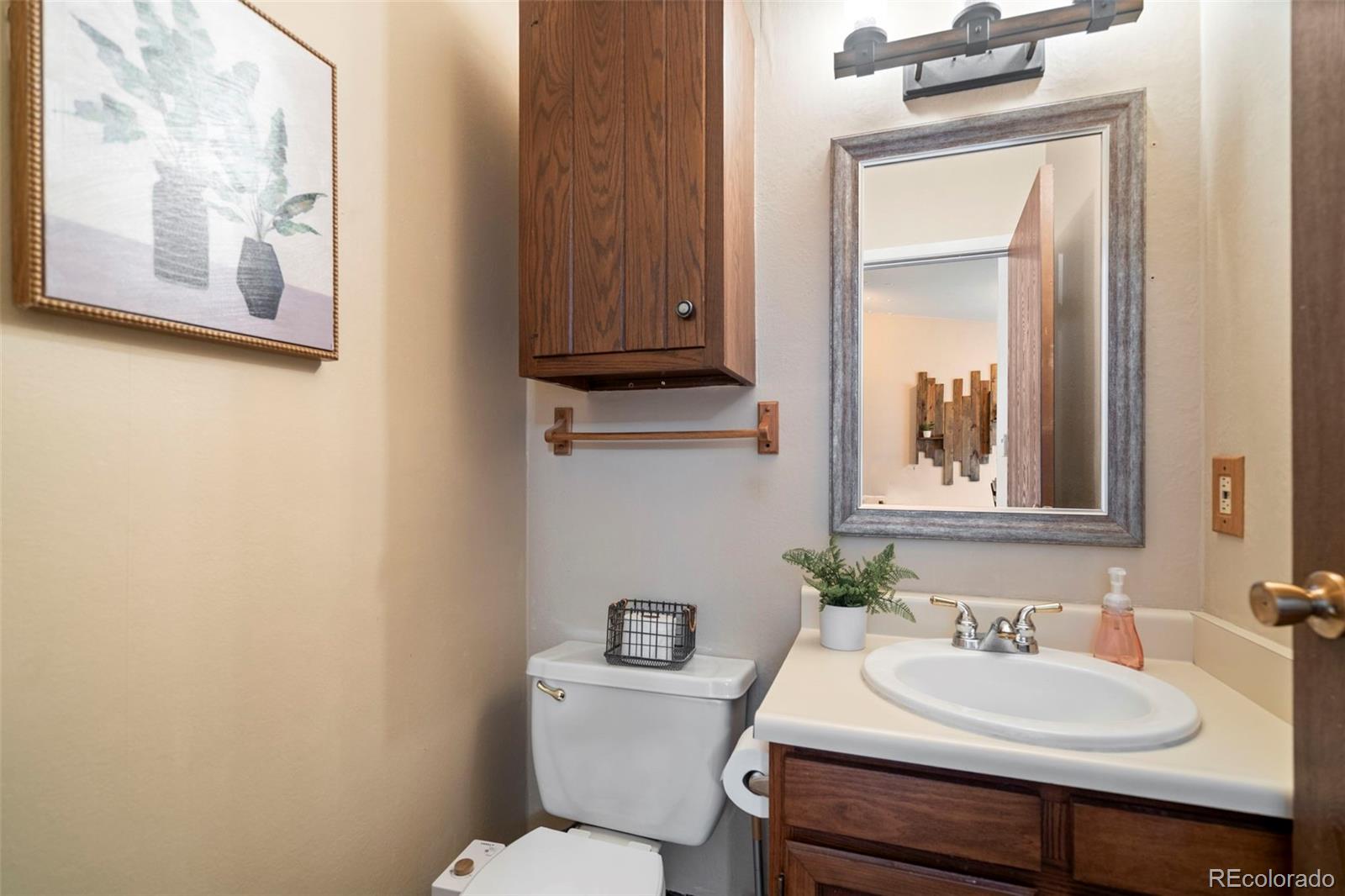 Bathroom with a wood vanity, white sink, toilet, and framed mirror.