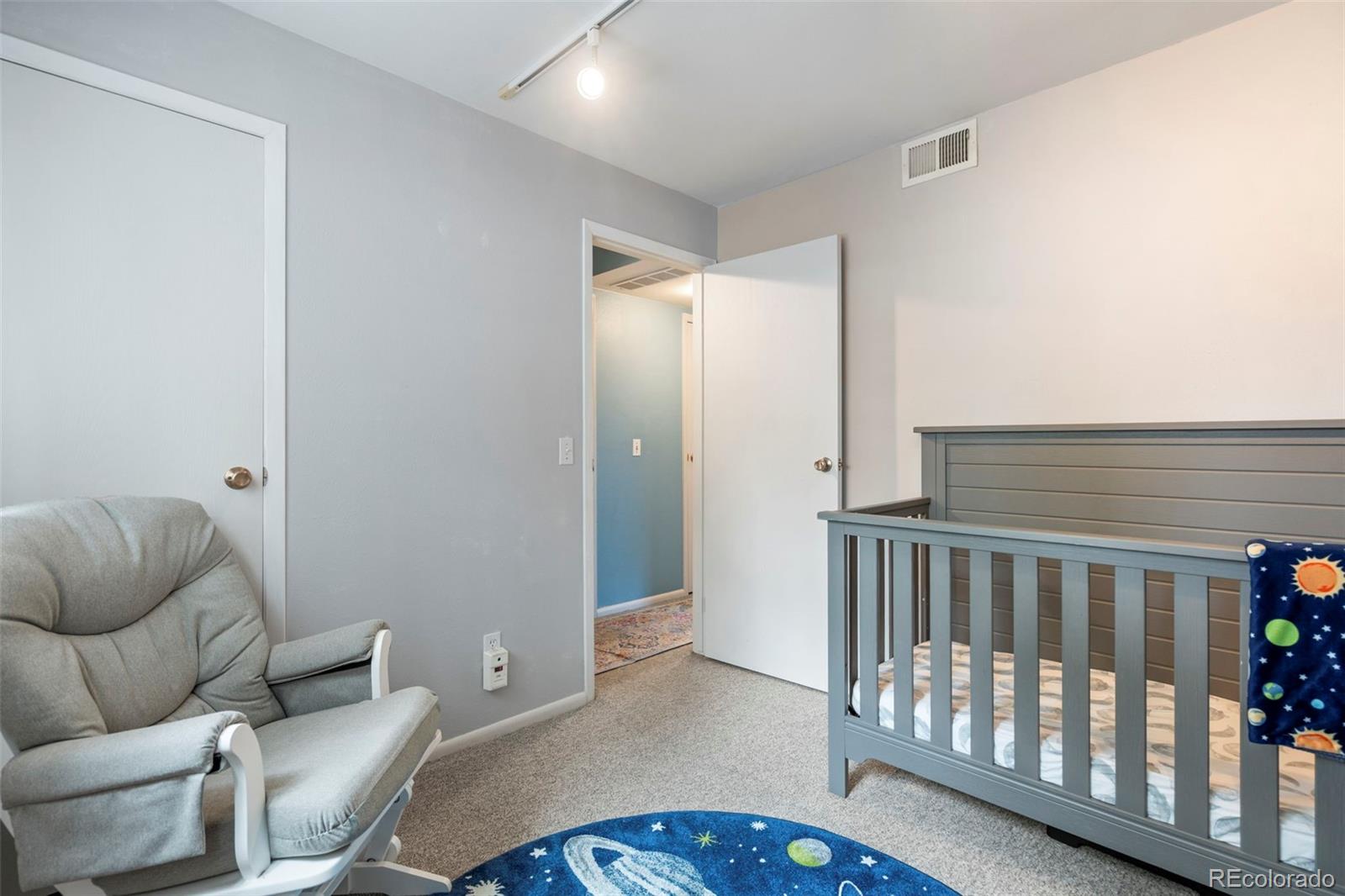 Bedroom with a gray child-sized bed, space-themed rug, and recliner.