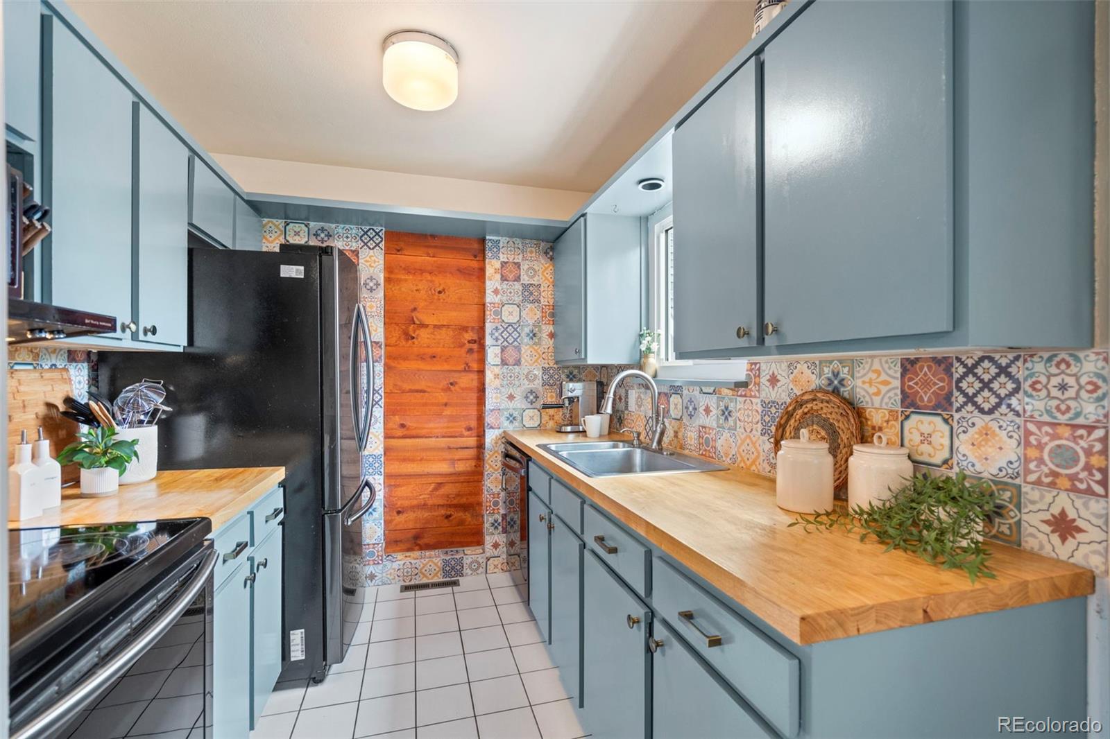 Kitchen with blue-gray cabinets, butcher-block counters, and a colorful patterned tile backsplash.