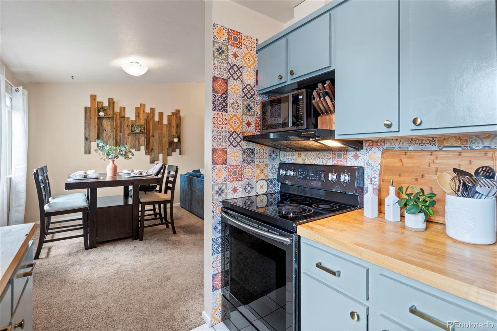 Kitchen and dining area with blue cabinets, patterned tile backsplash, and butcher-block counter.