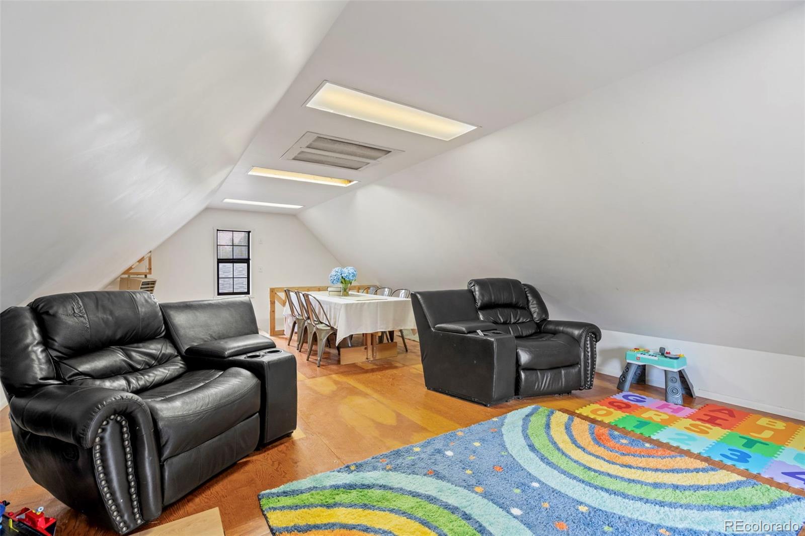Loft living room with black leather seating, a dining table, and colorful rugs on wood flooring.