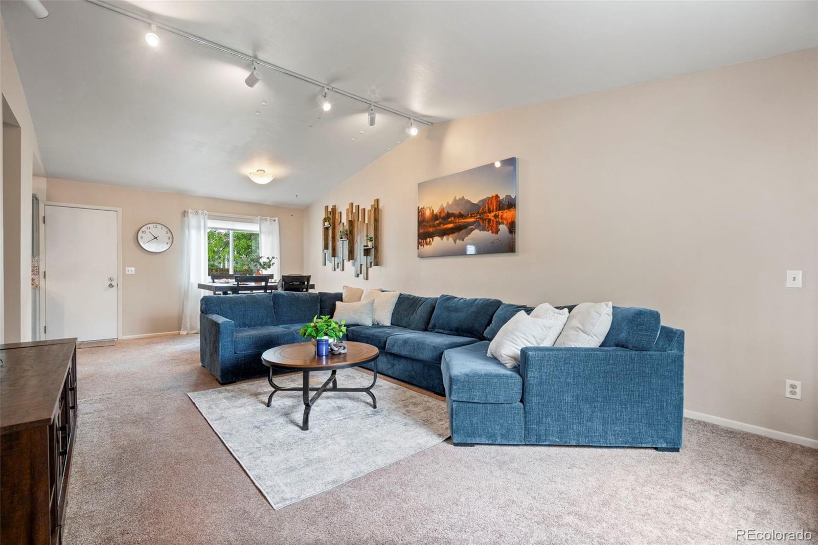 Living room with a blue sectional, round coffee table, pale rug, and dining area by the window.