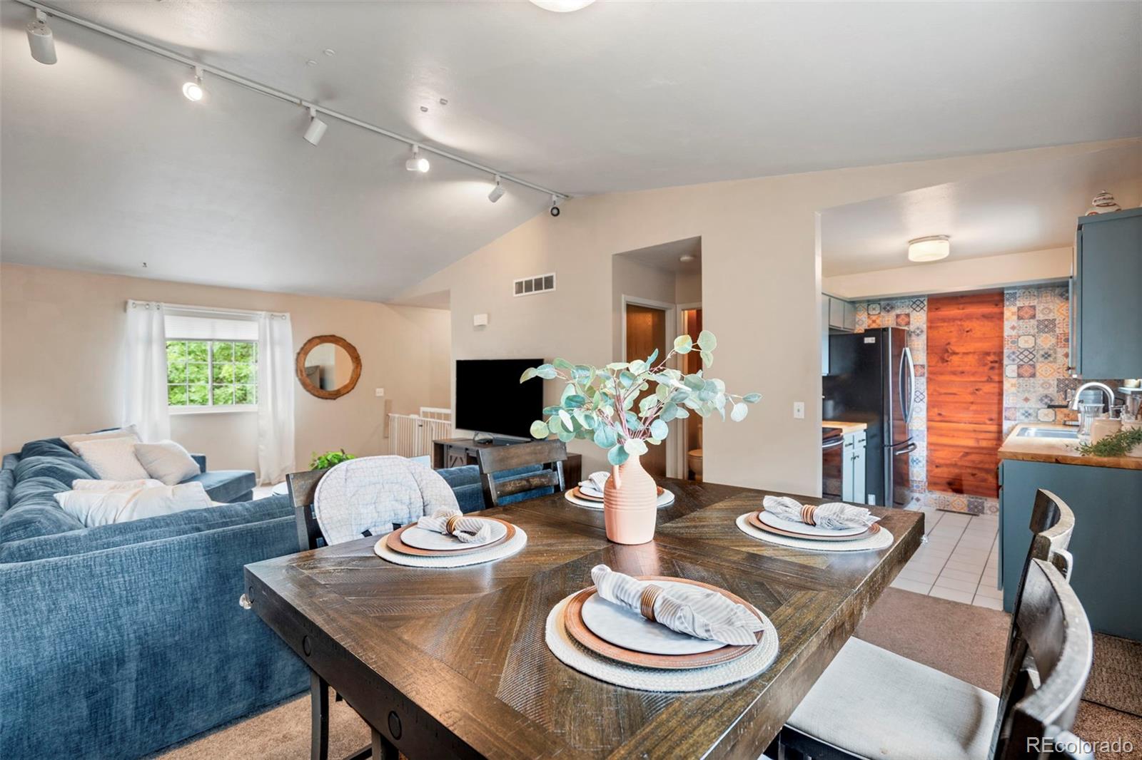 Dining area with a set dark wood table, adjoining blue living room and kitchen.