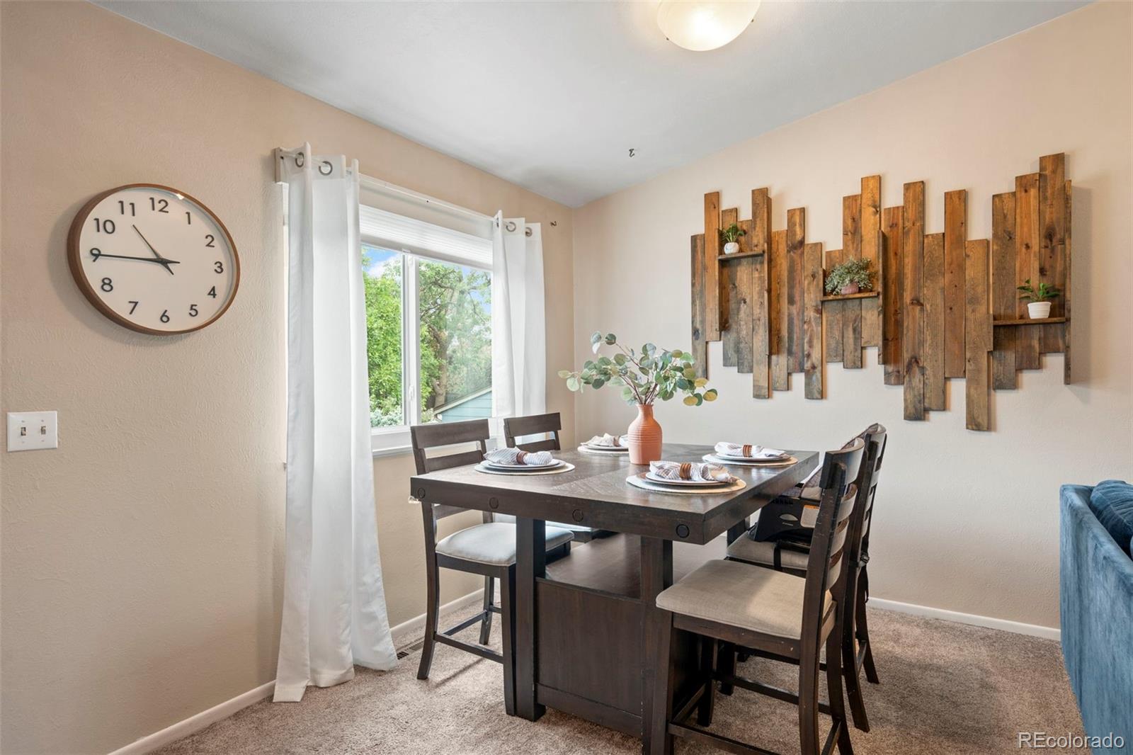 Dining room with a set table, large curtained window, and rustic wooden wall art.