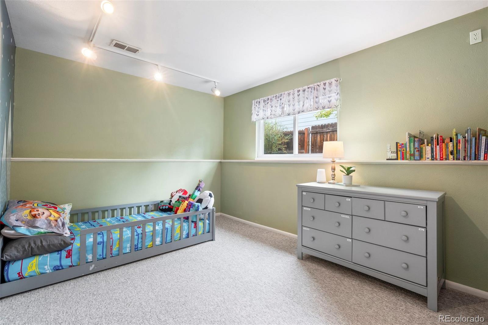 Nursery with a gray crib and dresser, sage green walls, and light carpet.