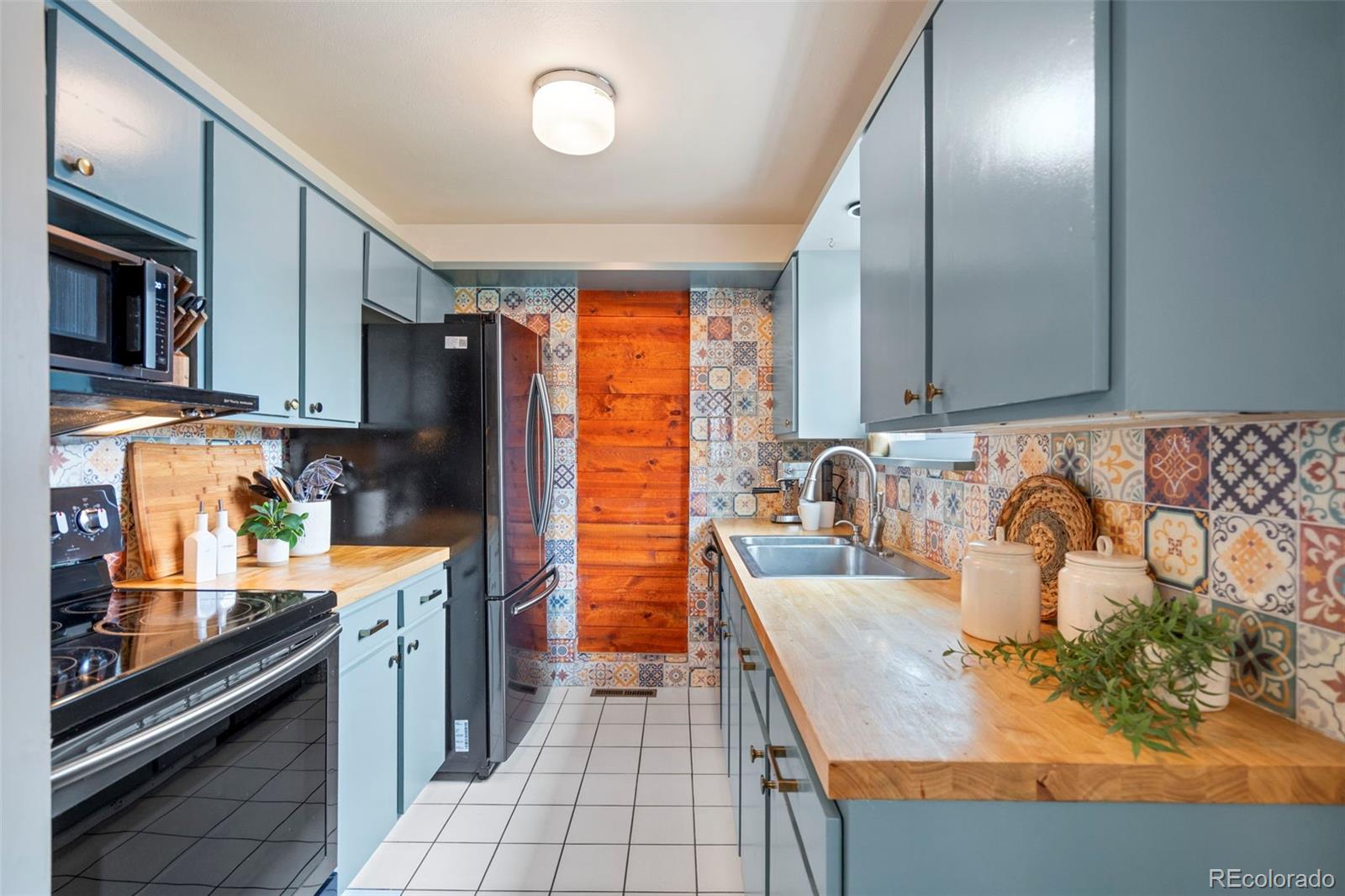 Galley kitchen with blue cabinets, patterned tile backsplash, and butcher-block countertops.