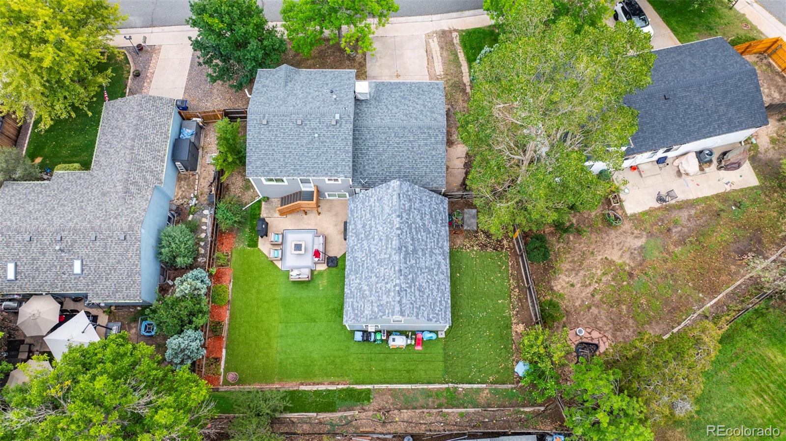 Aerial view of a home’s green backyard, furnished patio, and mature trees.