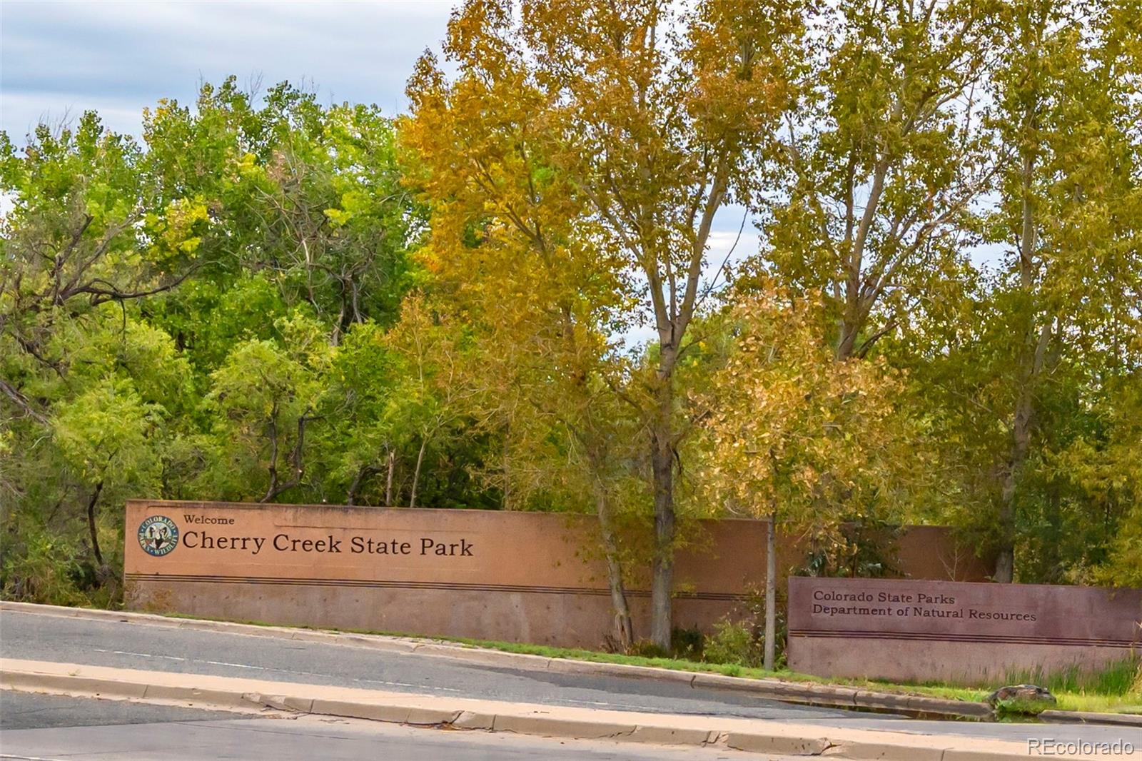 Cherry Creek State Park entrance sign beneath autumn trees beside the road.