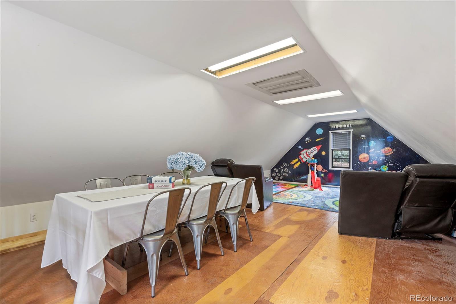Furnished attic bonus room with sloped ceilings, leather seating, and a colorful space-themed play area.