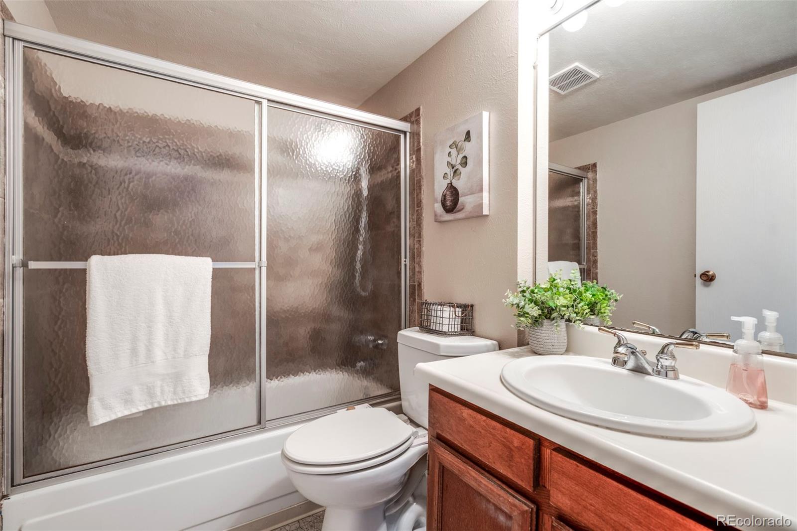 Bathroom with frosted-glass shower doors, white sink, and reddish wood vanity.