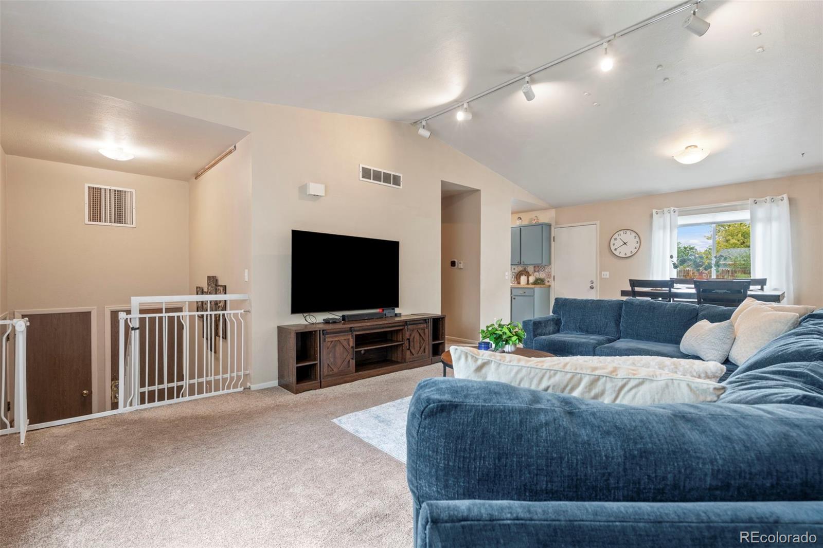 Living room with vaulted ceiling, blue sectional sofa, and television beside an open dining area.