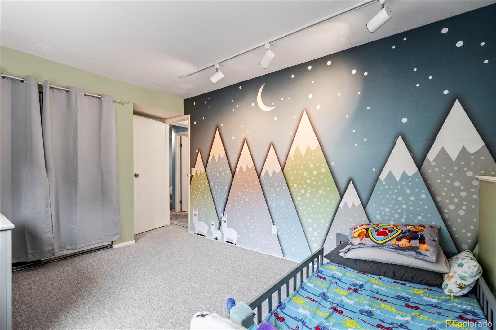 Child’s bedroom with a colorful mountain-and-moon mural behind a bed.