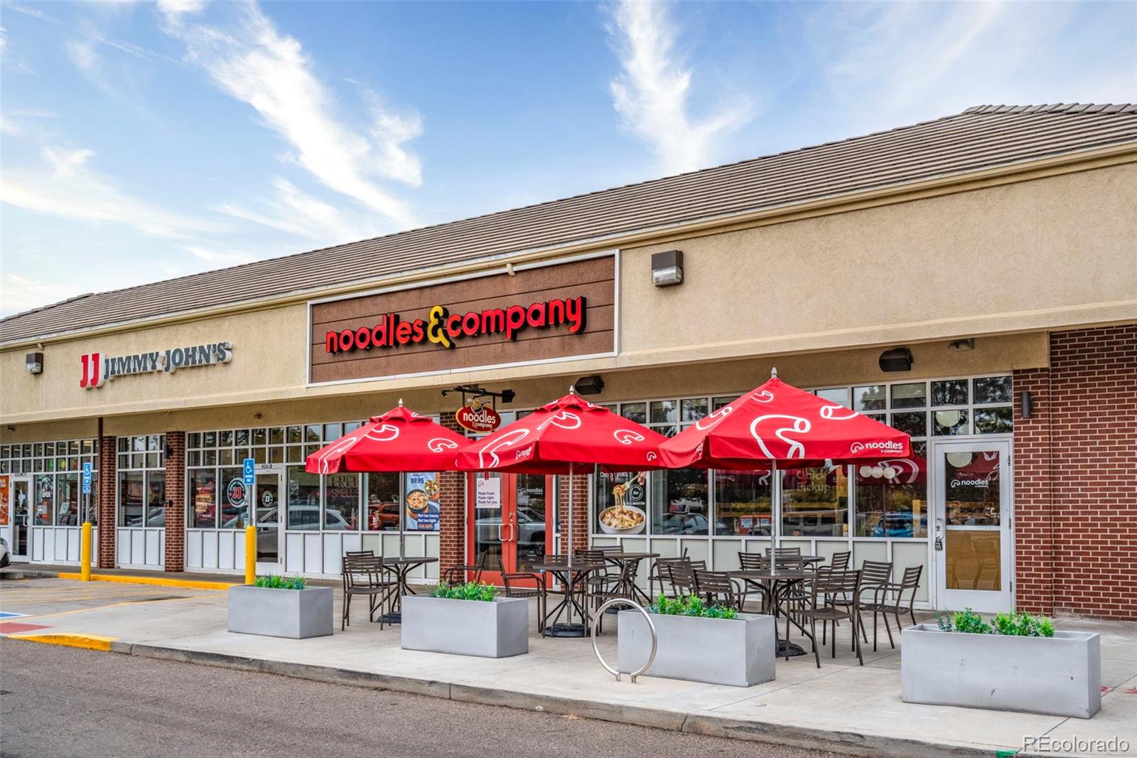 Restaurant storefronts with red patio umbrellas and outdoor dining tables along the sidewalk.