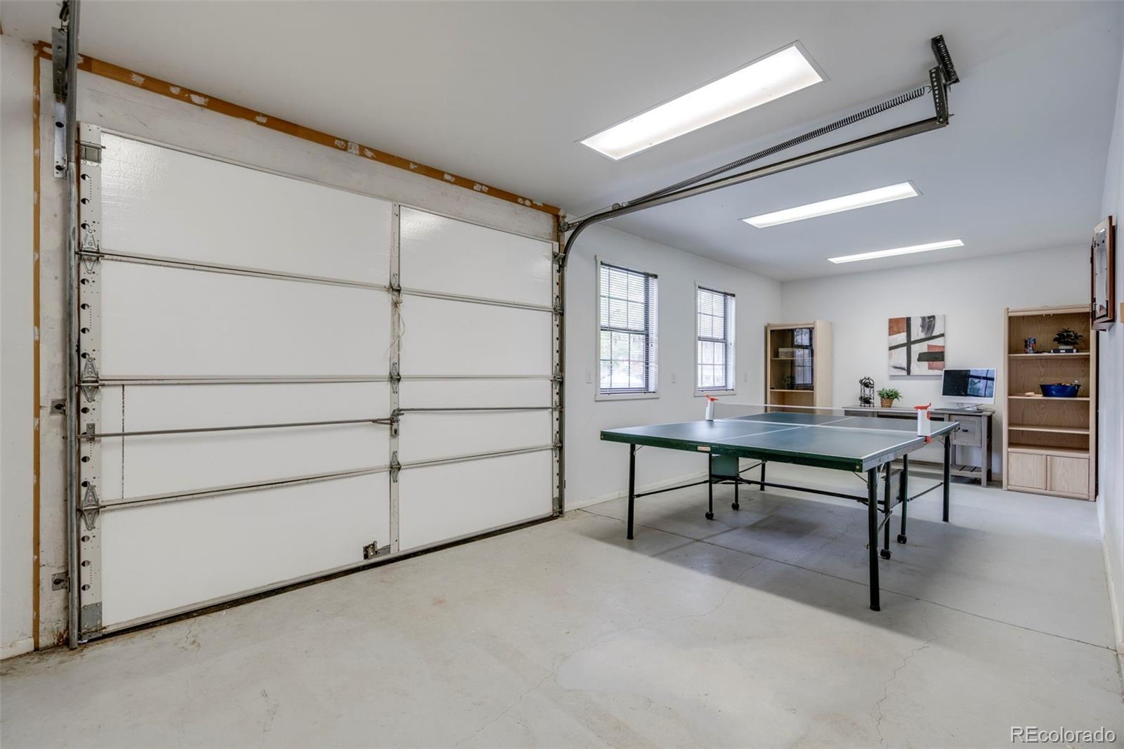 Garage with a green ping-pong table, white overhead door, and shelving along the back wall.