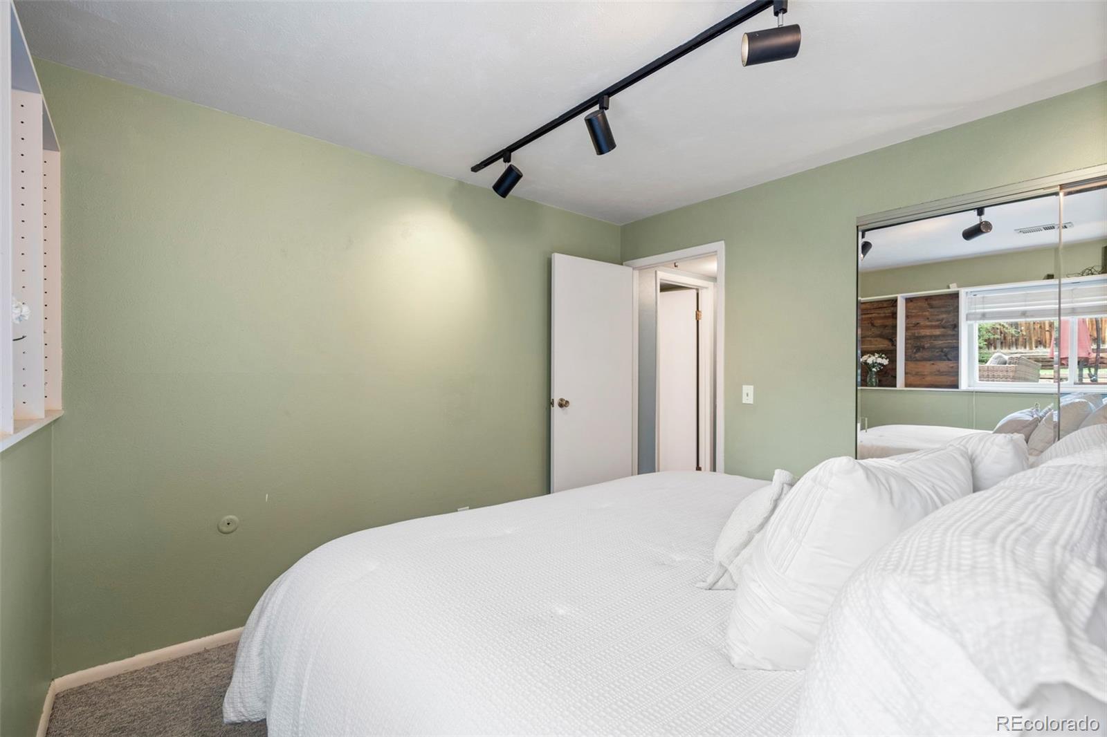Bedroom with a large white bed, pale green walls, and mirrored closet doors.