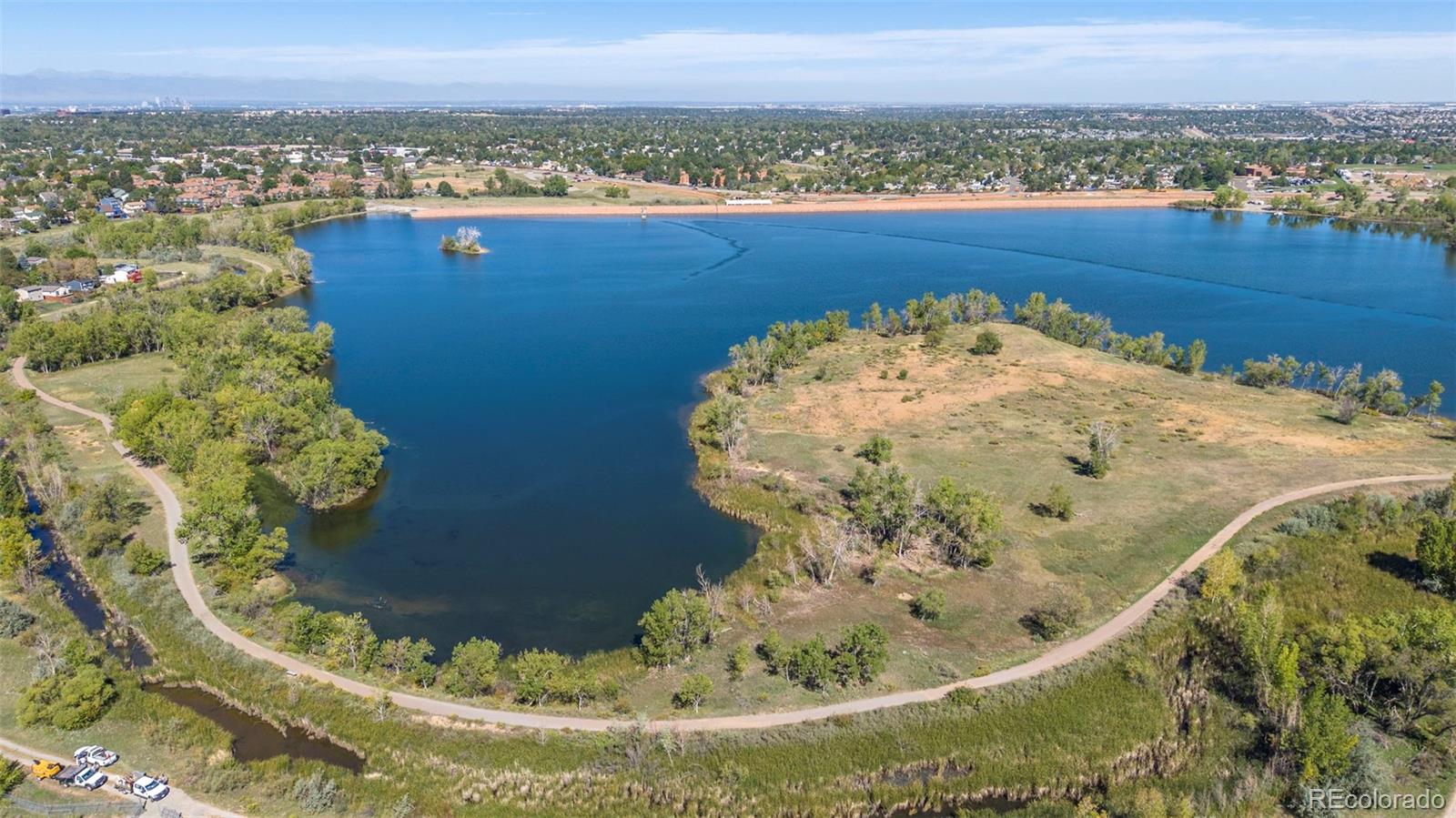 Aerial view of a blue lake surrounded by tree-lined paths and open green space.