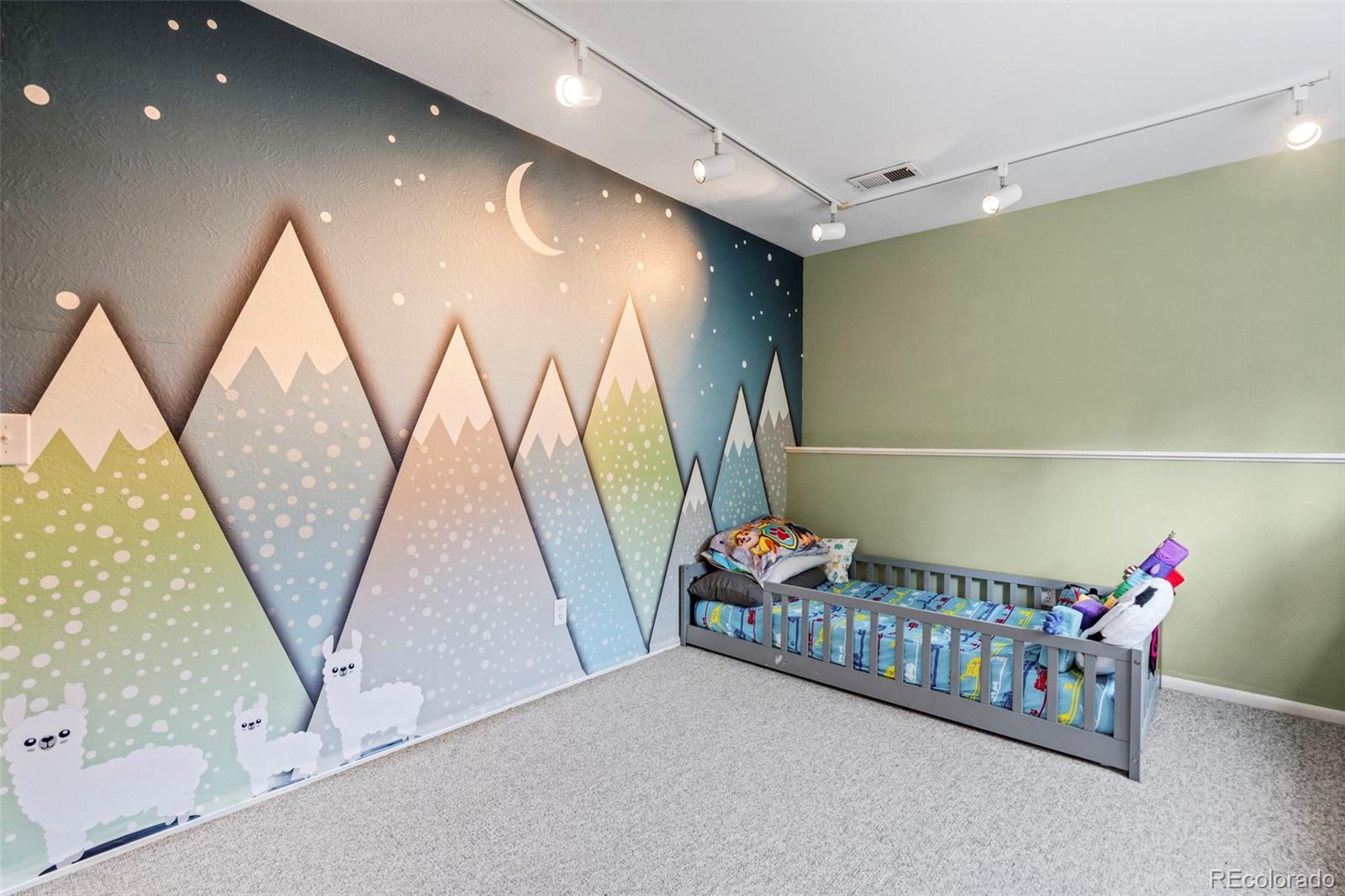 Bedroom with a gray toddler bed and a colorful mountain, moon, and llama mural.