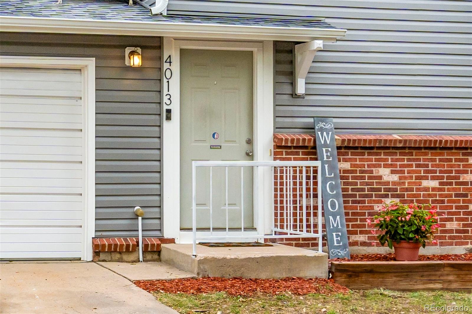 Home entrance with white door and railing, brick wall, and a tall welcome sign.
