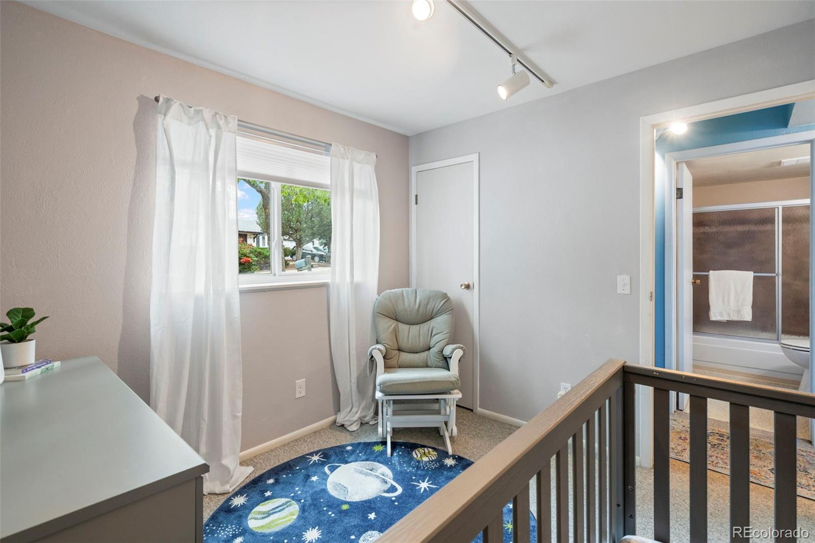 Upstairs sitting area with a gray armchair, space-themed rug, and bathroom doorway.