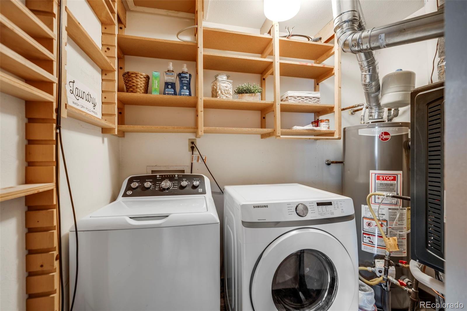 Laundry room with two white washers, a water heater, and extensive wooden shelving.