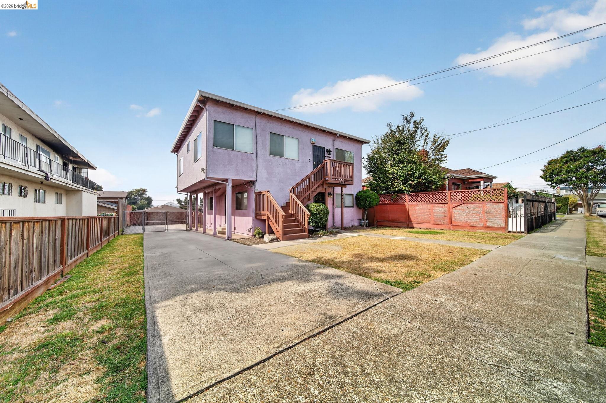 Pink two-story residence with exterior staircases, driveway, and fenced front yard.