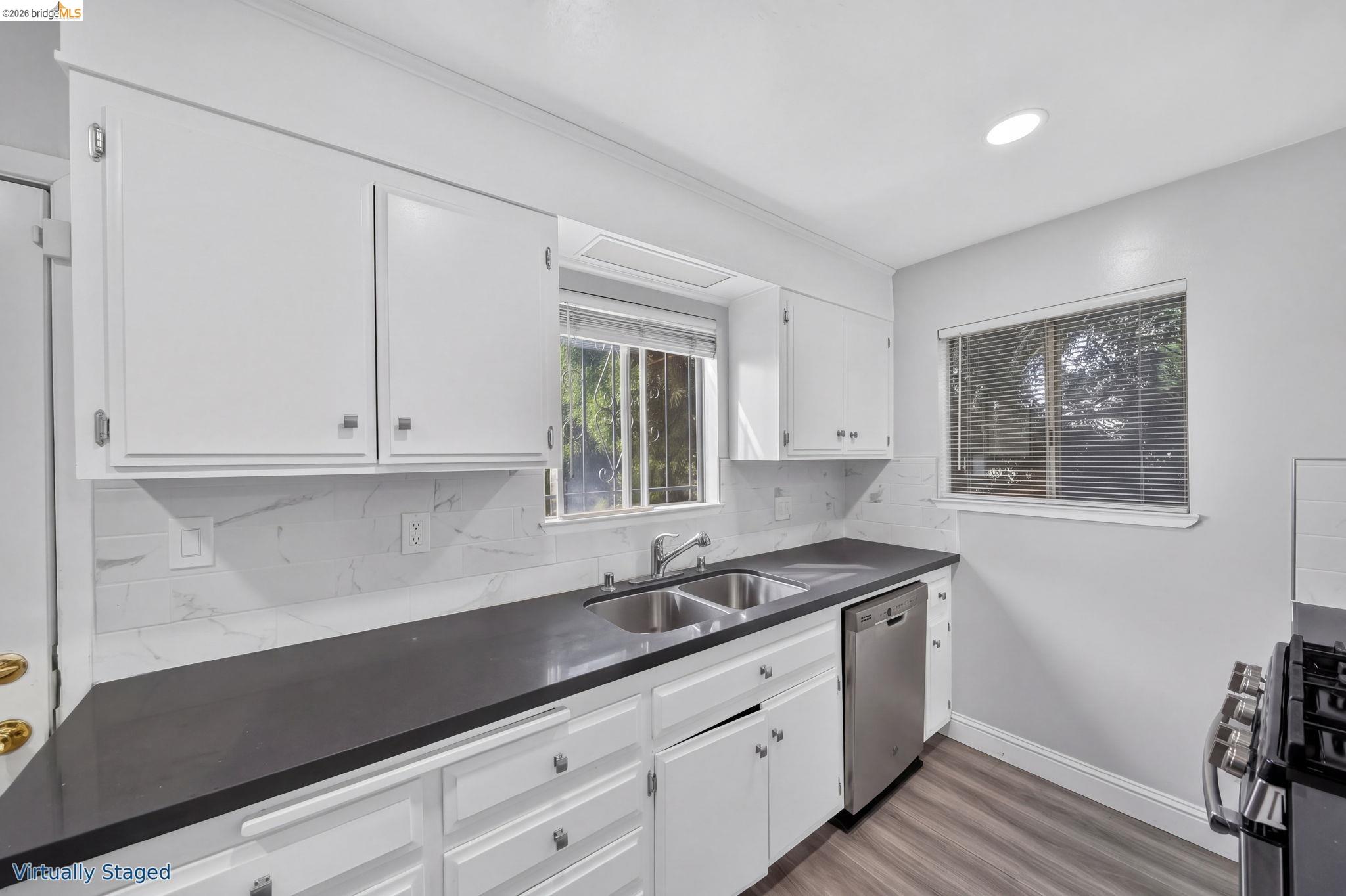 Kitchen with white cabinets, dark countertops, marble-look backsplash, double sink, and stainless steel appliances.