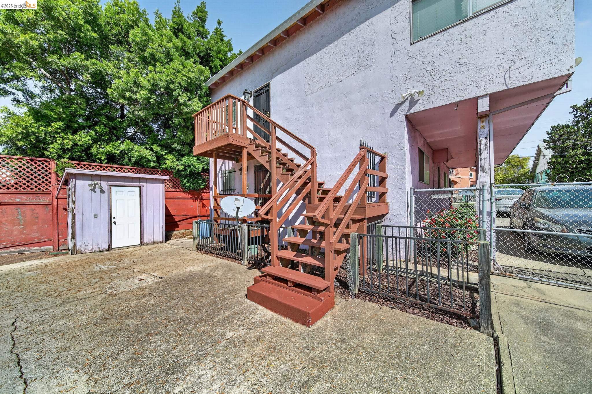 Rear of a two-story stucco house with wooden exterior stairs, landings, and a small shed.