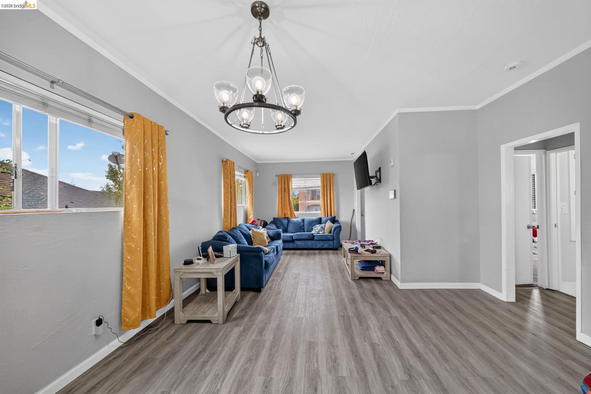 Living room with blue sofas, mustard curtains, large windows, and gray wood-look flooring.