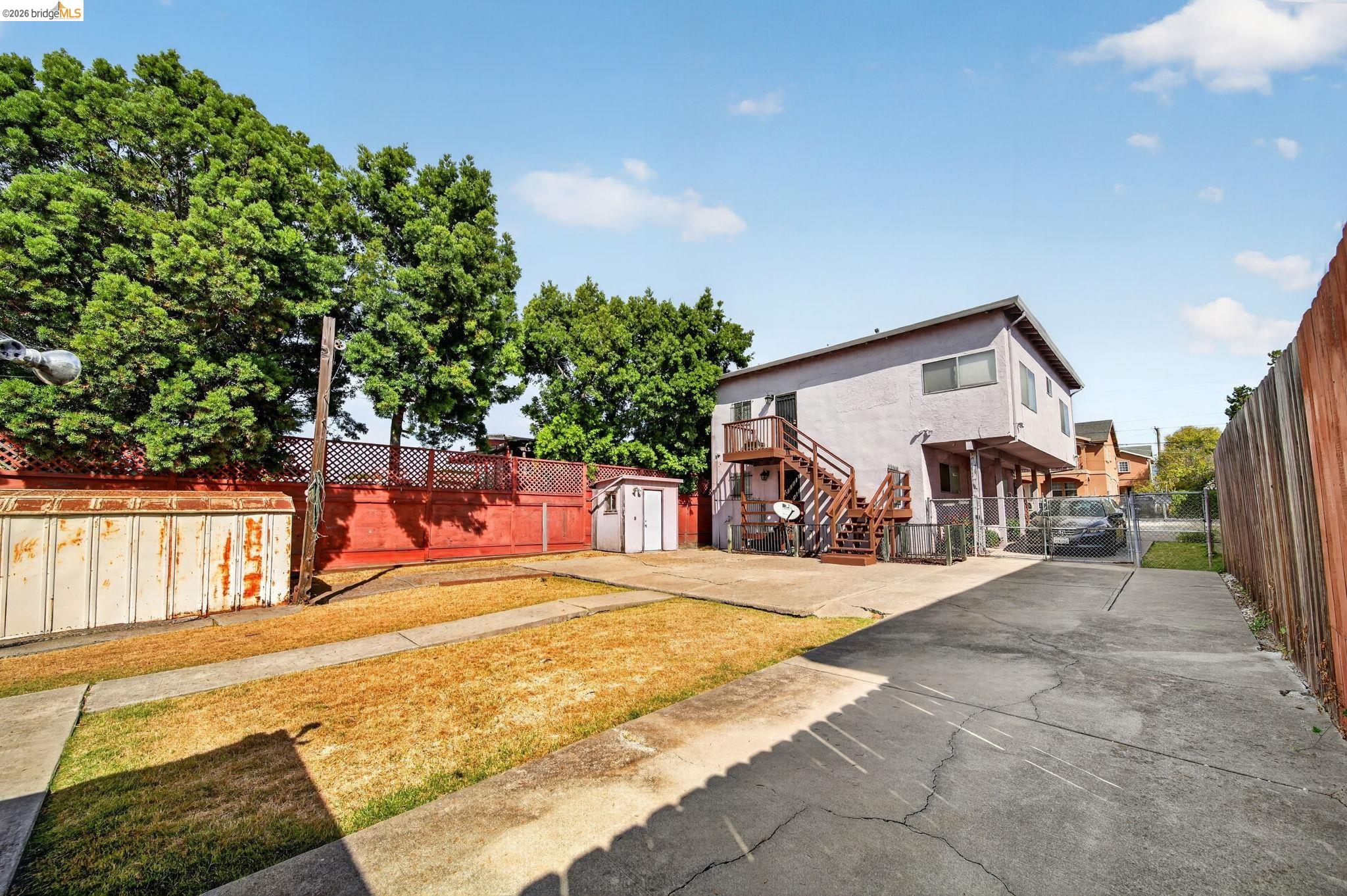 Rear of a two-story home with exterior stairs, a fenced yard, and a wide concrete driveway.