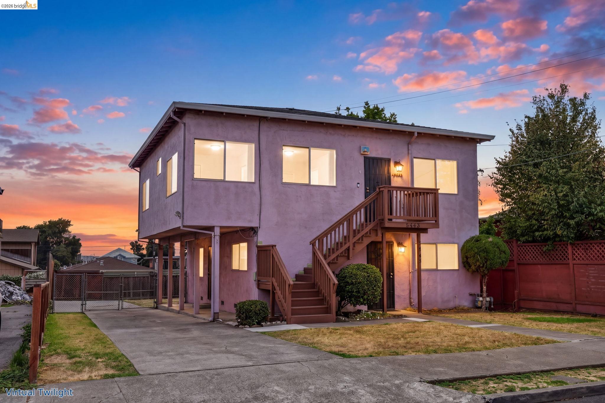 Two-story home with exterior staircases and glowing windows beneath a pink-clouded twilight sky.
