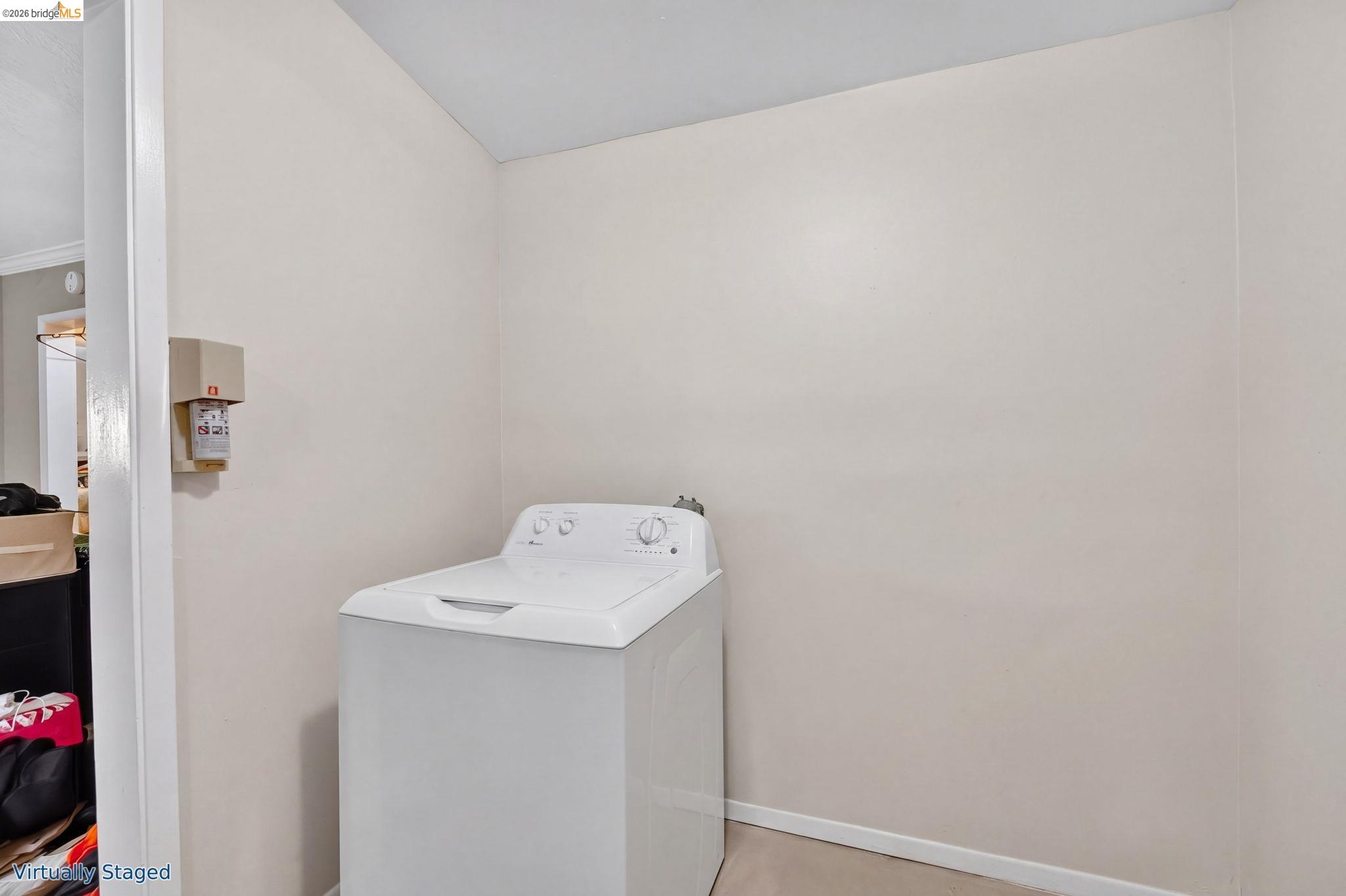 Laundry room with a white top-loading washer and beige walls.