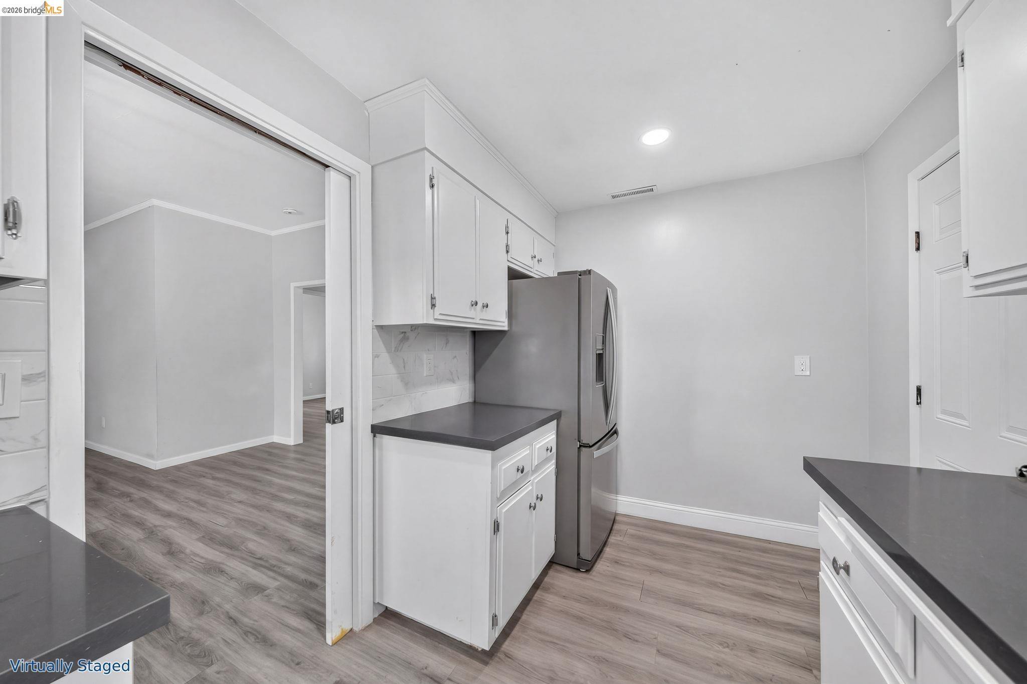 Vacant kitchen with white cabinetry, dark countertops, and a stainless-steel refrigerator.