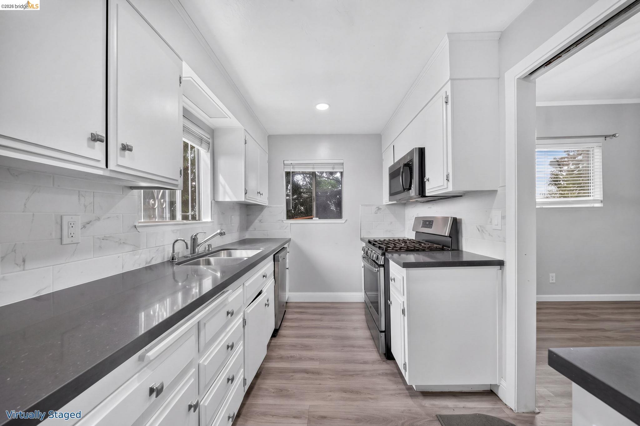 Galley kitchen with white cabinets, gray counters, marble-look backsplash, and stainless steel appliances.
