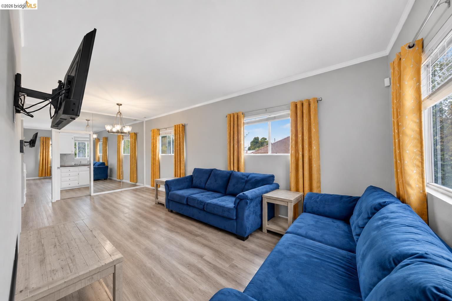 Living room with blue sofas, mustard curtains, and light wood flooring.