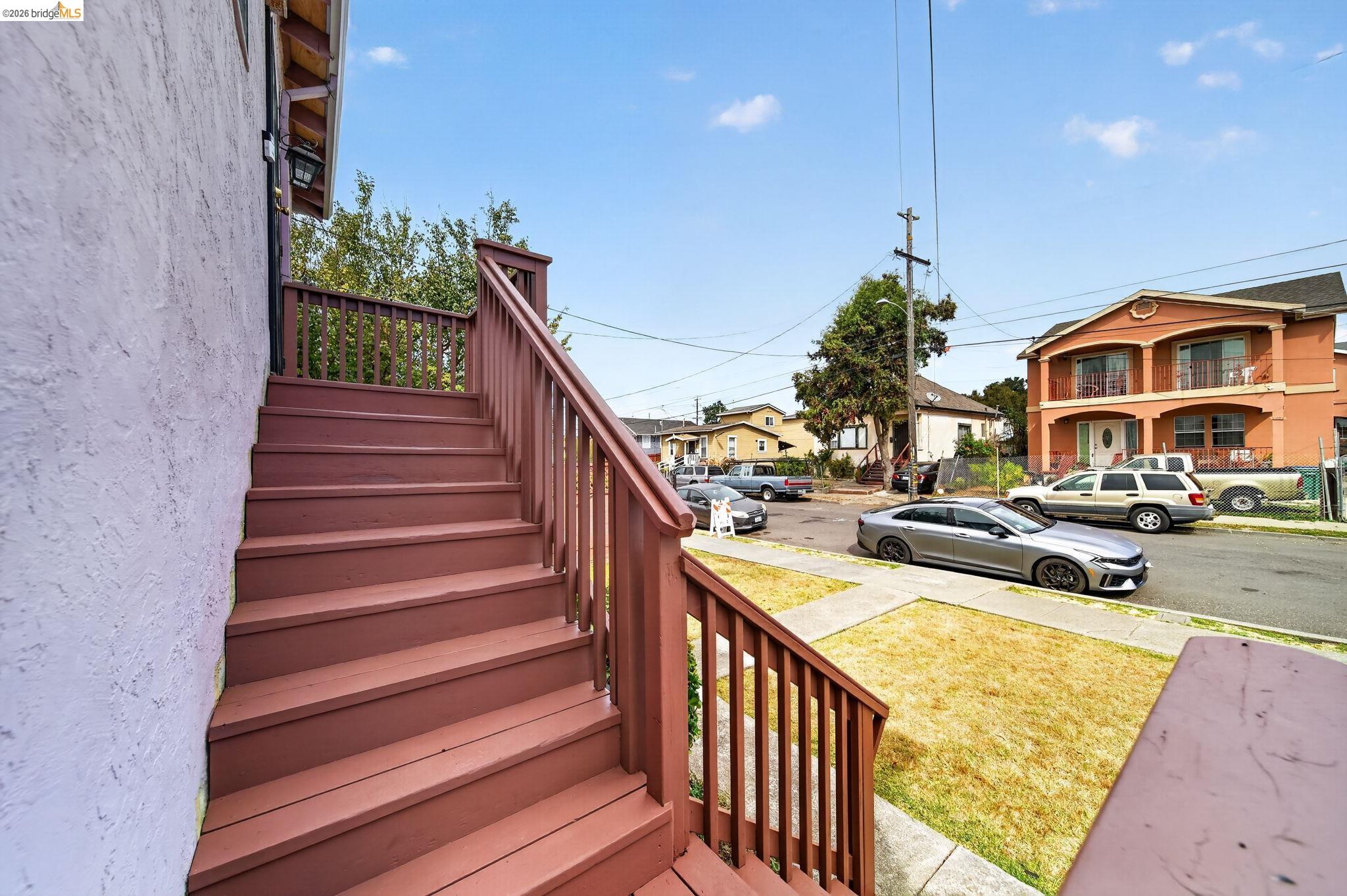 Wooden entry stairs overlook a dry front lawn and a residential street with parked cars.