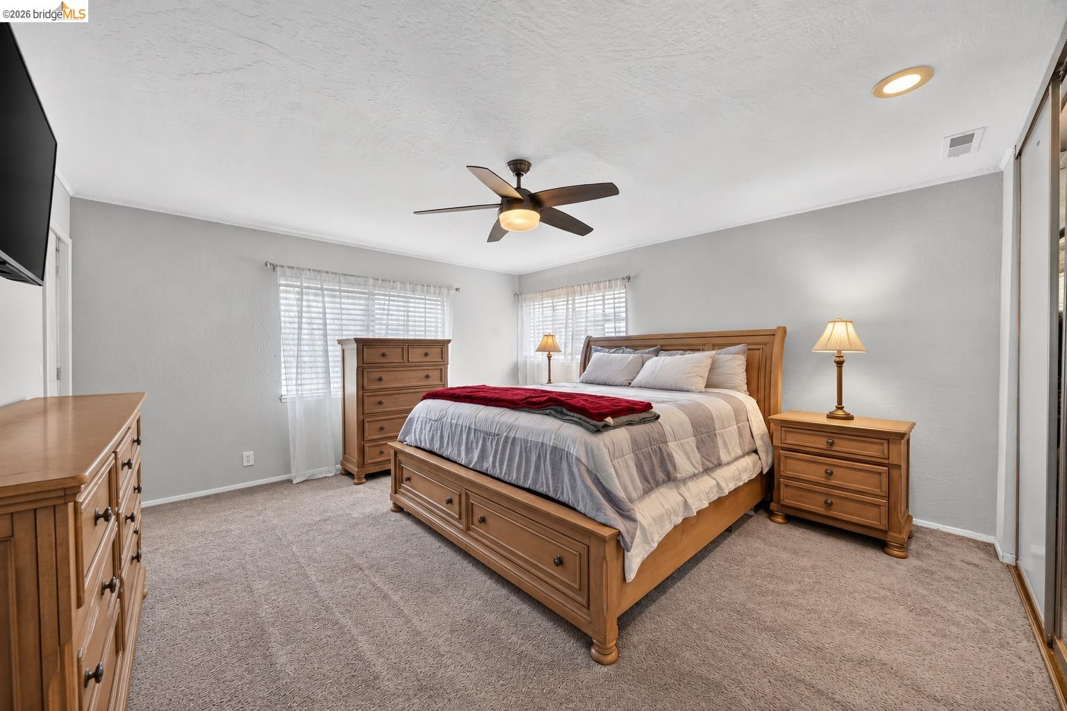 Furnished bedroom with a wooden bed, matching dressers, red throw, and ceiling fan.