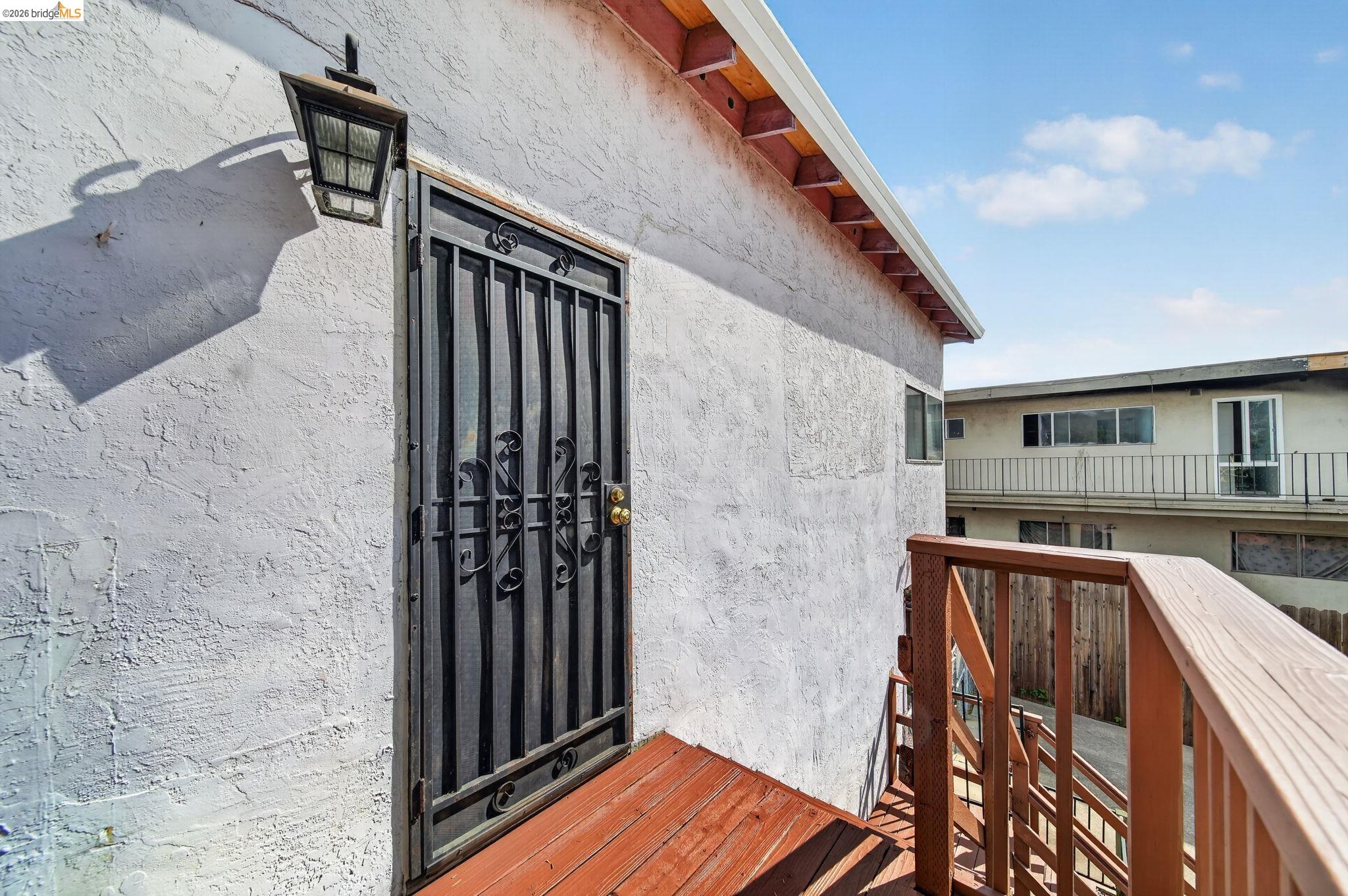Raised wooden entry deck with a black security door and lantern on a white stucco house.