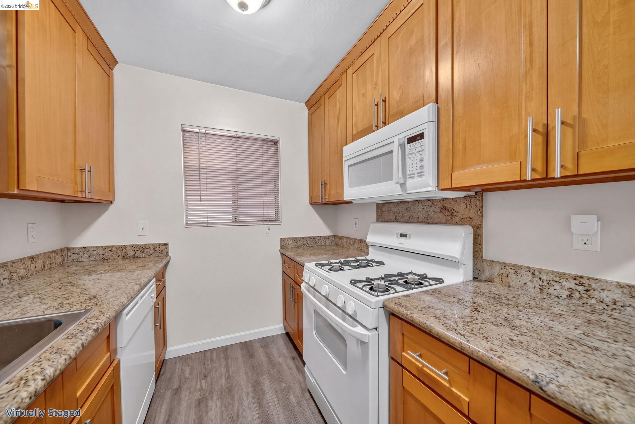 Kitchen with honey-colored cabinets, granite counters, and white gas range and microwave.