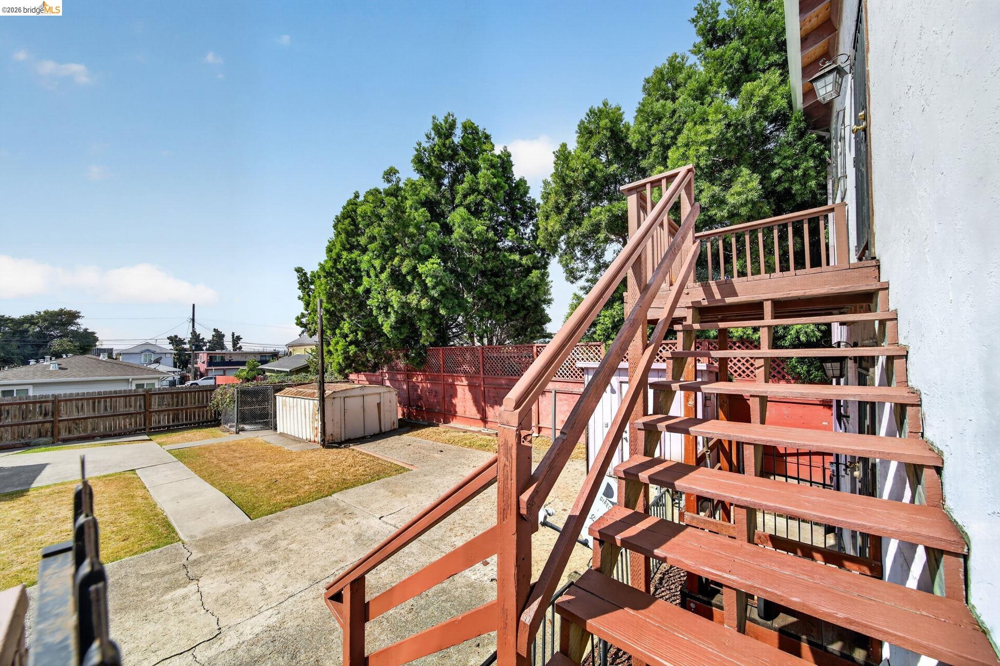 Fenced backyard with a large wooden exterior staircase, concrete paths, and a storage shed.