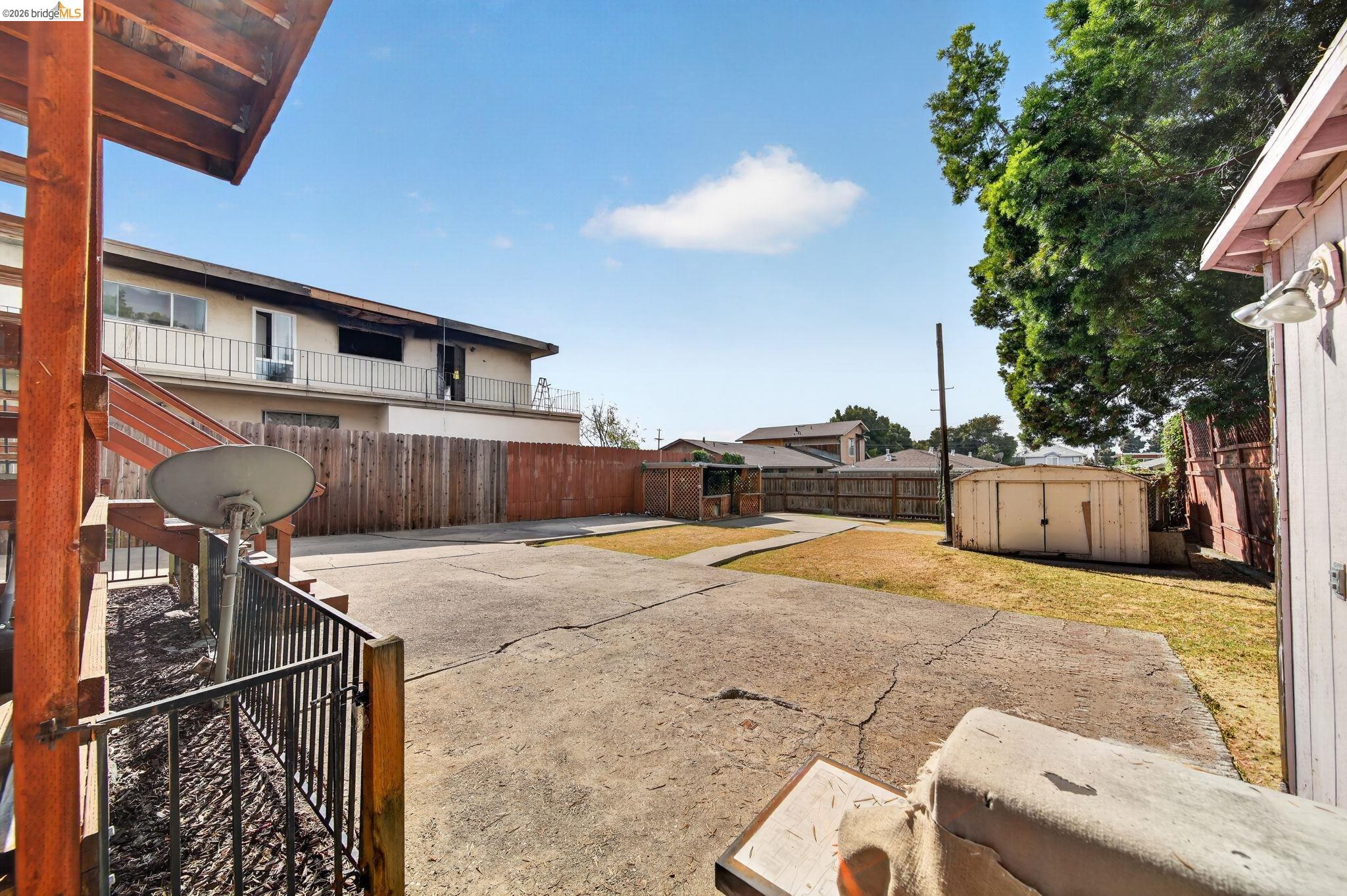 Fenced backyard with a broad concrete patio, patchy lawn, storage shed, and covered wooden deck.