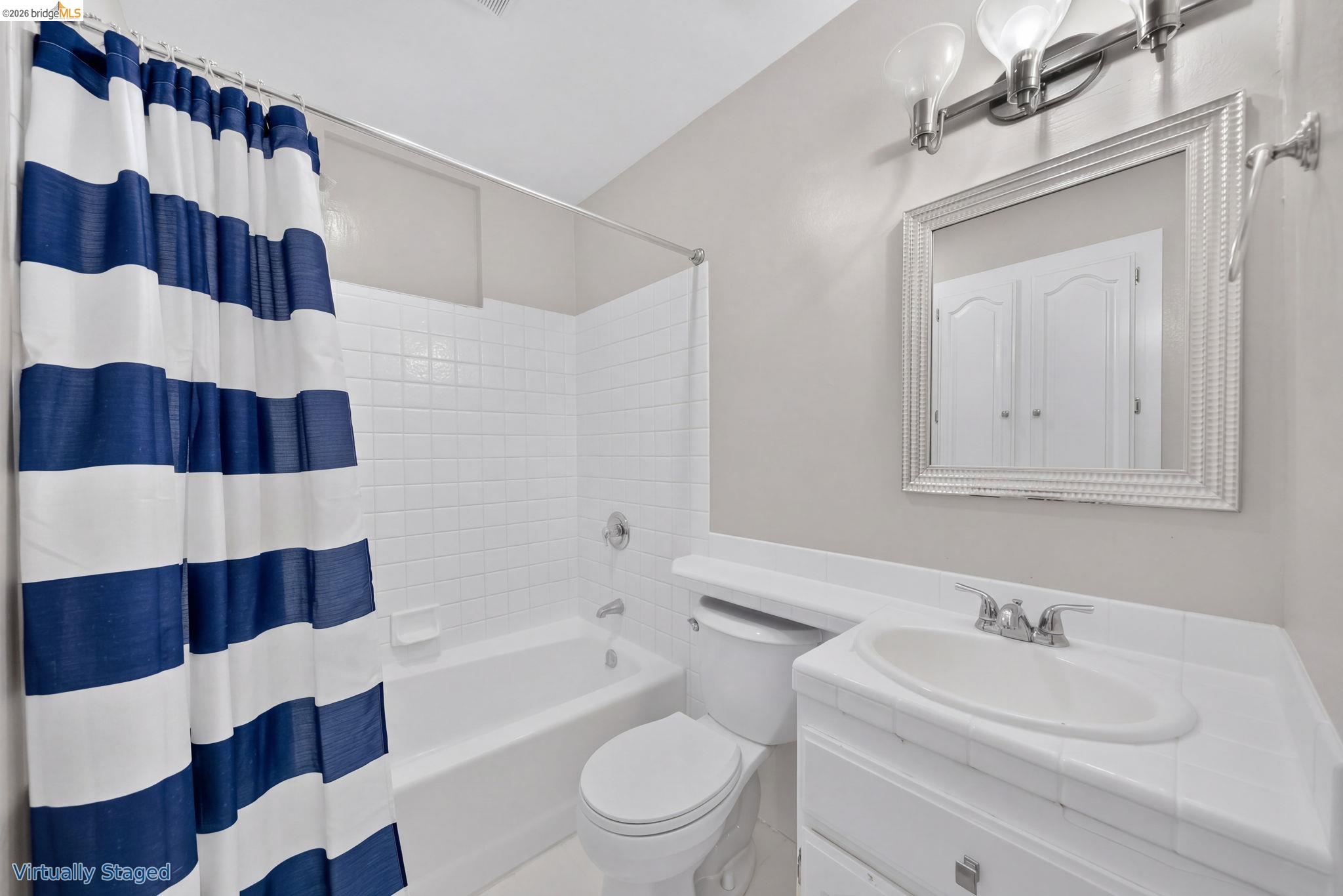Bathroom with a navy-and-white striped shower curtain, white tub, toilet, and vanity.