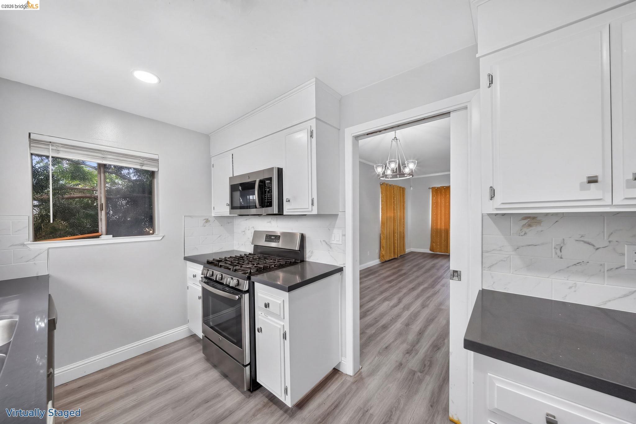 Virtually staged kitchen with white cabinets, dark counters, stainless steel range, and a doorway to the dining area.