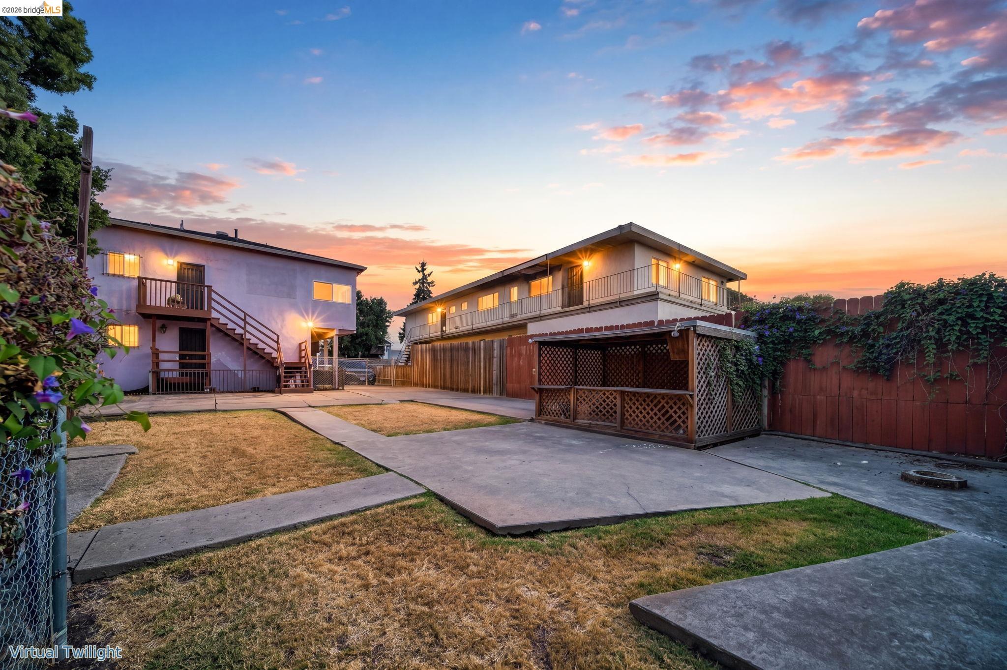 Two-story home and courtyard at dusk, with exterior stairs, balconies, and a wooden lattice gazebo.