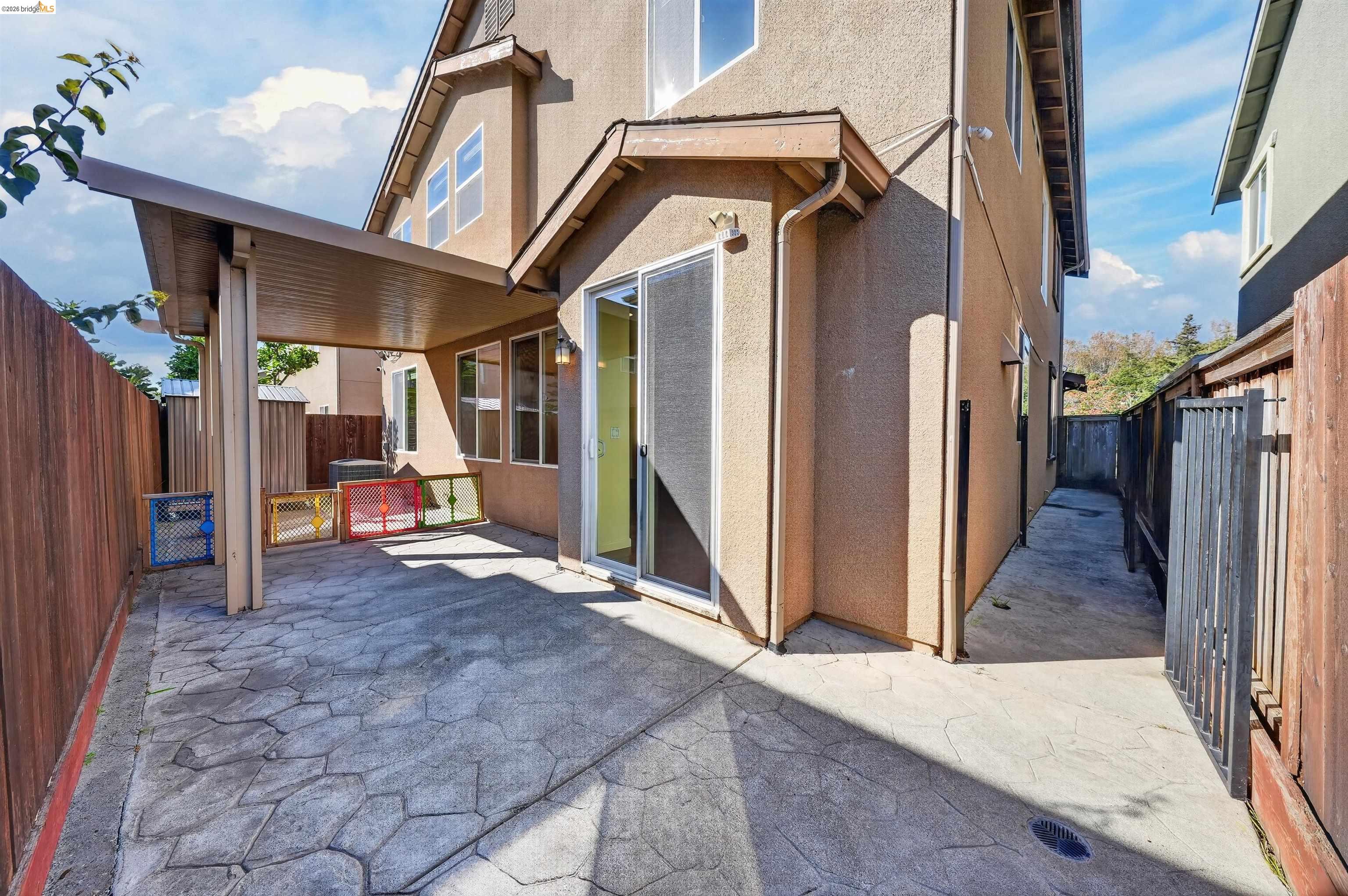 Back patio with stamped concrete, covered seating area, and fenced side passage.