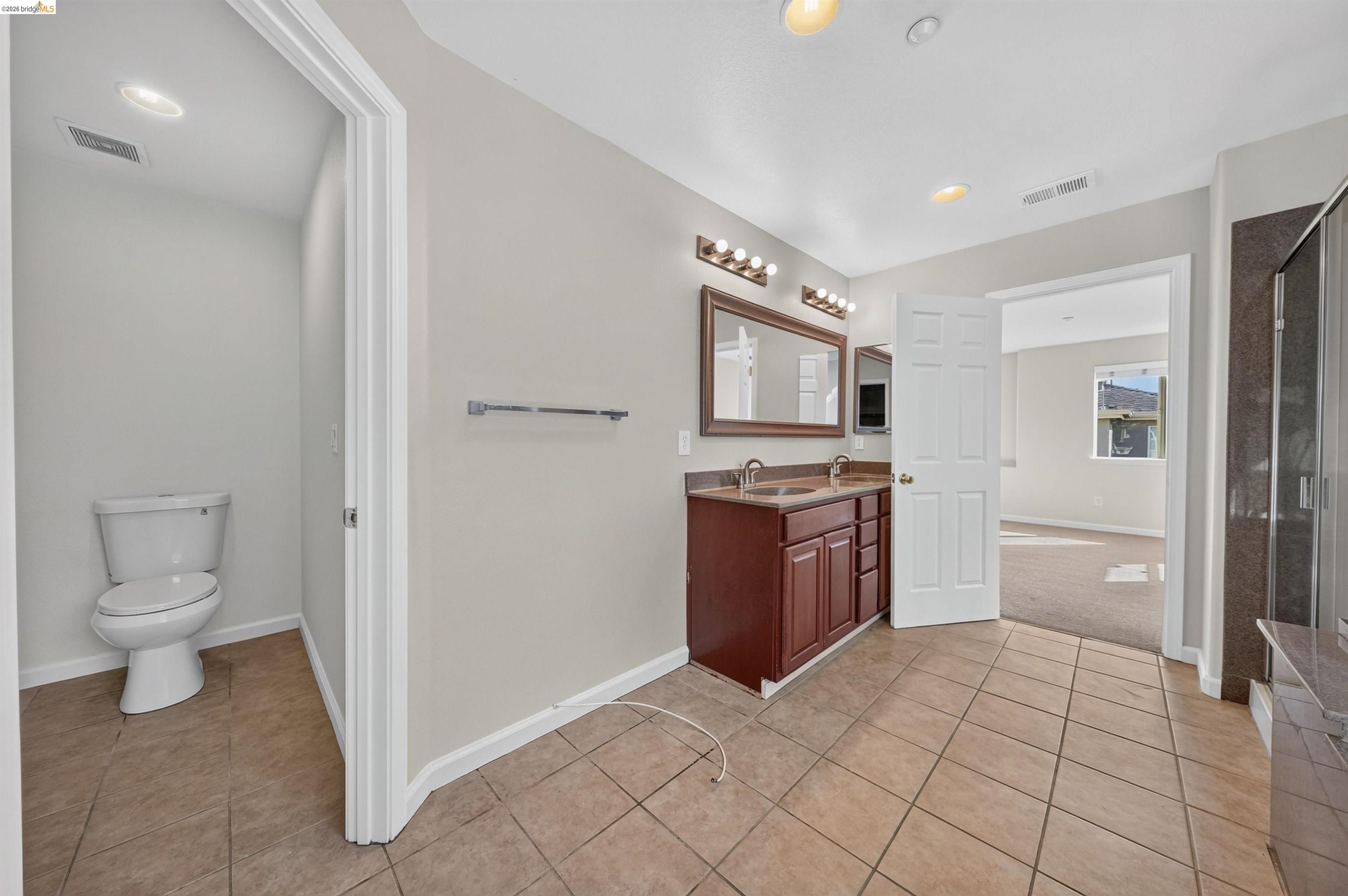 Bathroom with a double-sink vanity, separate toilet alcove, and tiled floor.