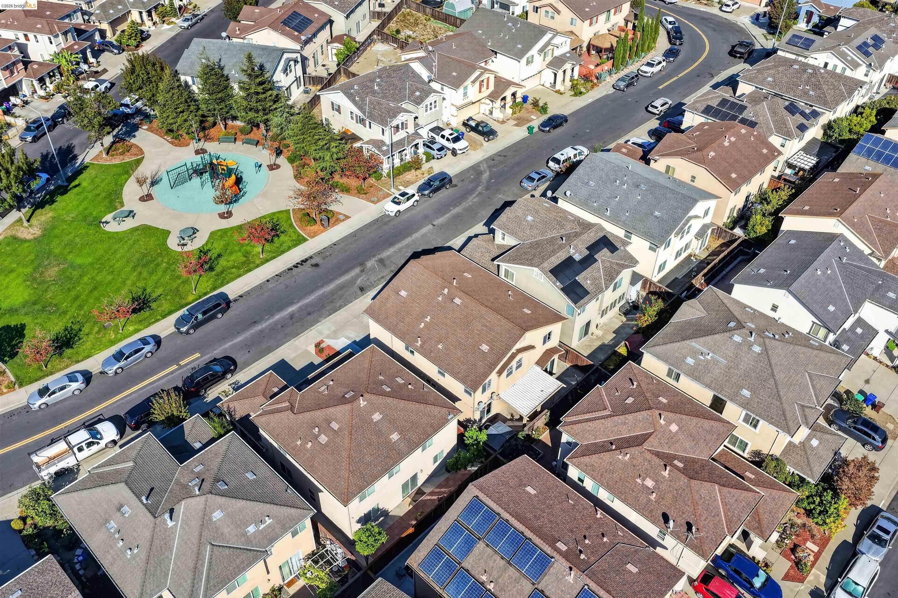 Aerial view of homes around a neighborhood park with a playground and solar-panel roofs.