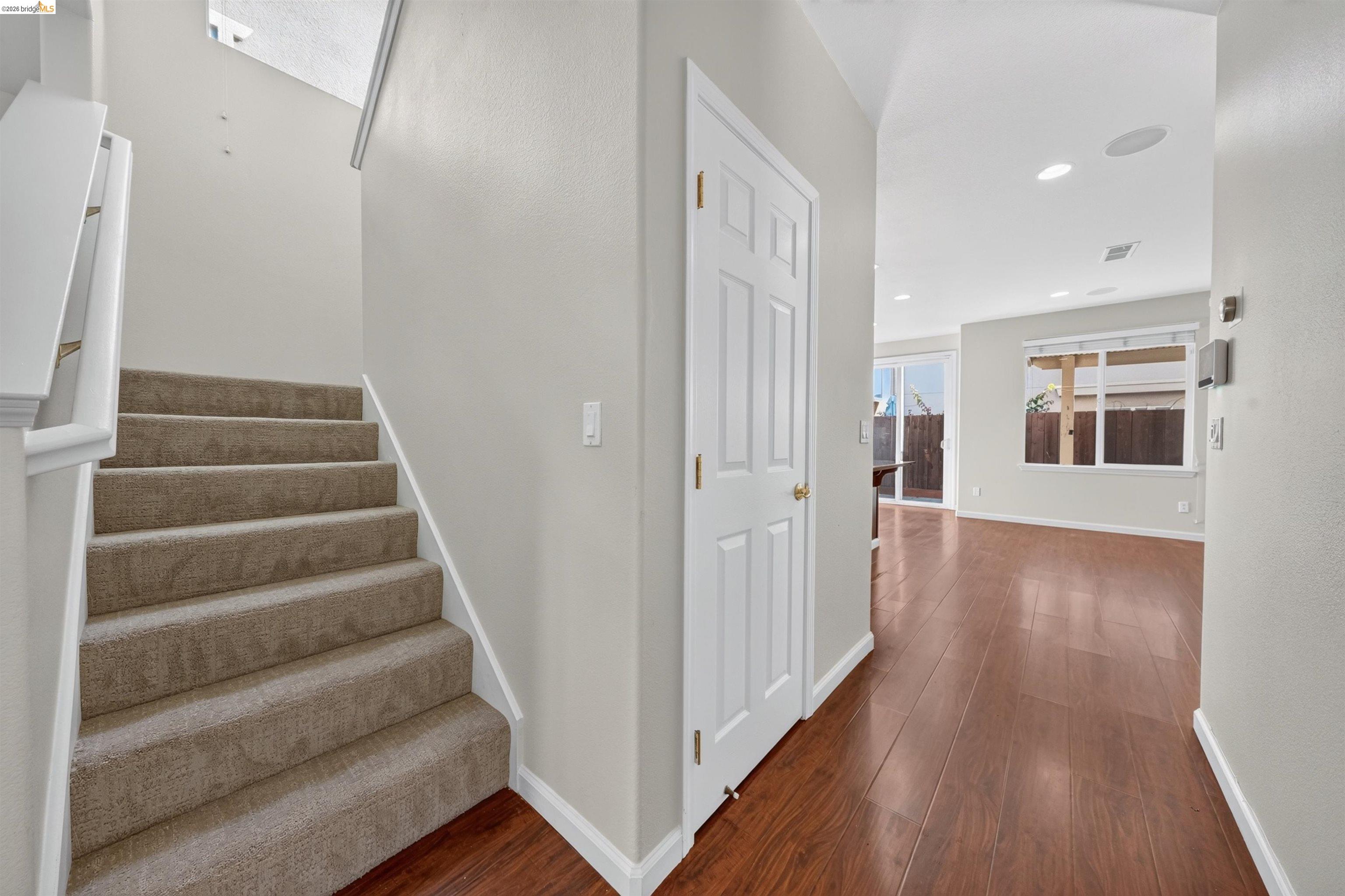 Entry hallway with carpeted stairs, white doors, and wood-look flooring.