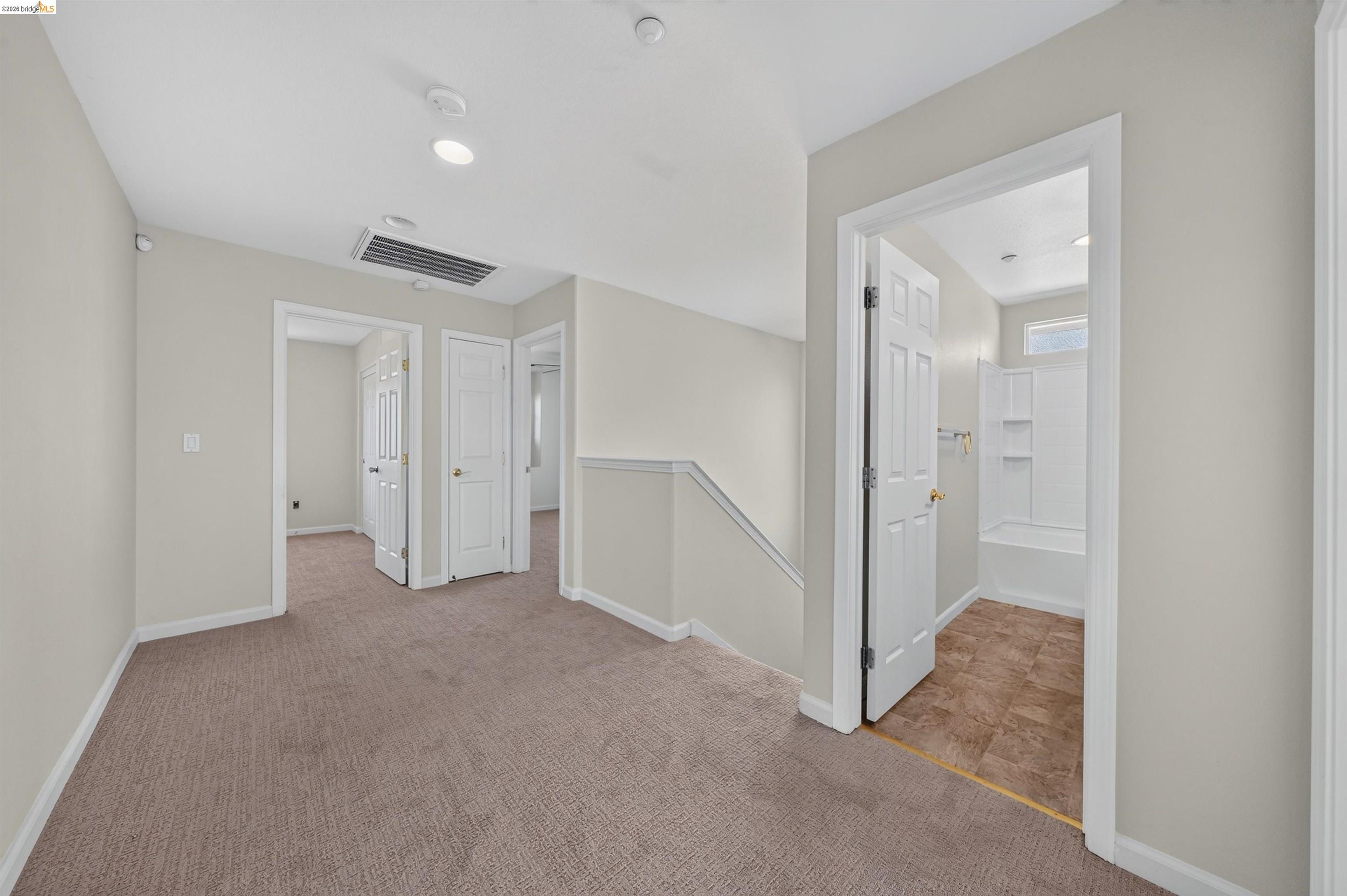 Carpeted upstairs landing with several doorways and an open bathroom featuring a tub-shower.